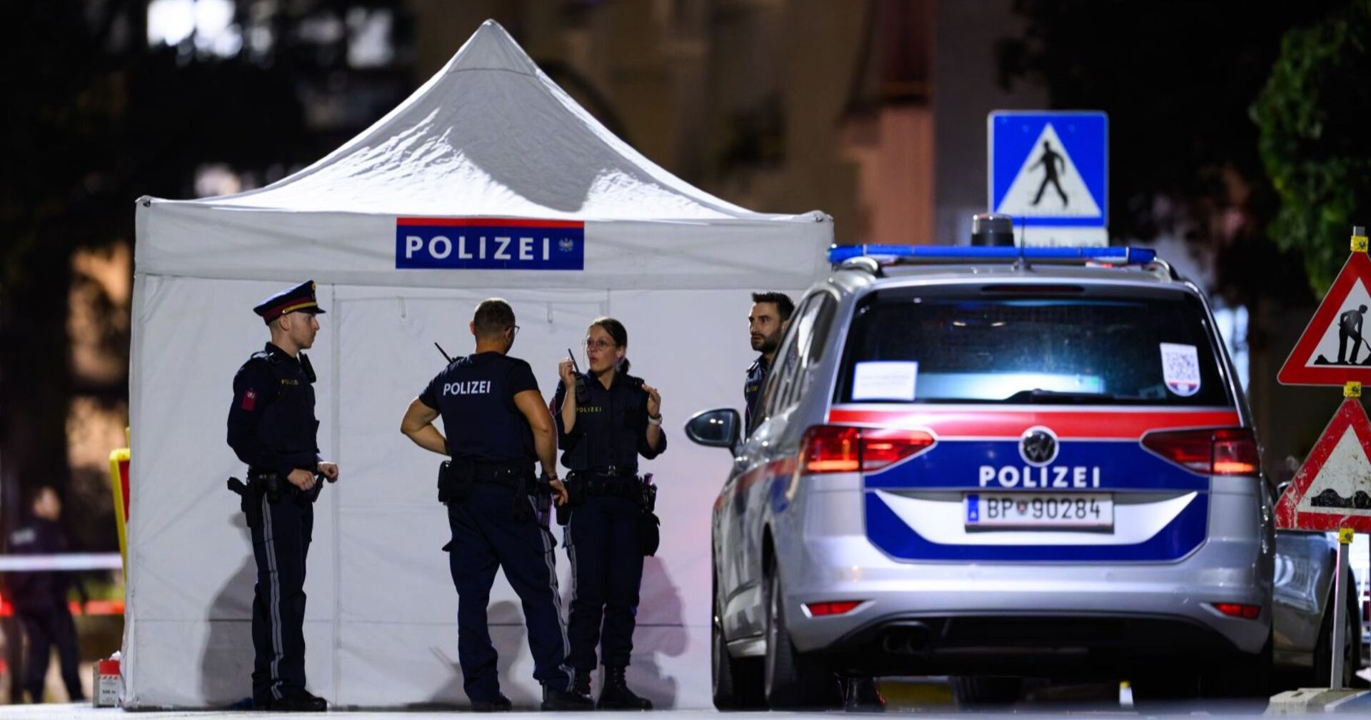 Polizisten vor einem weißen Sichtschutzzelt und einem Polizeiwagen am Tatort in Wien-Leopoldstadt nach der tödlichen Schießerei.