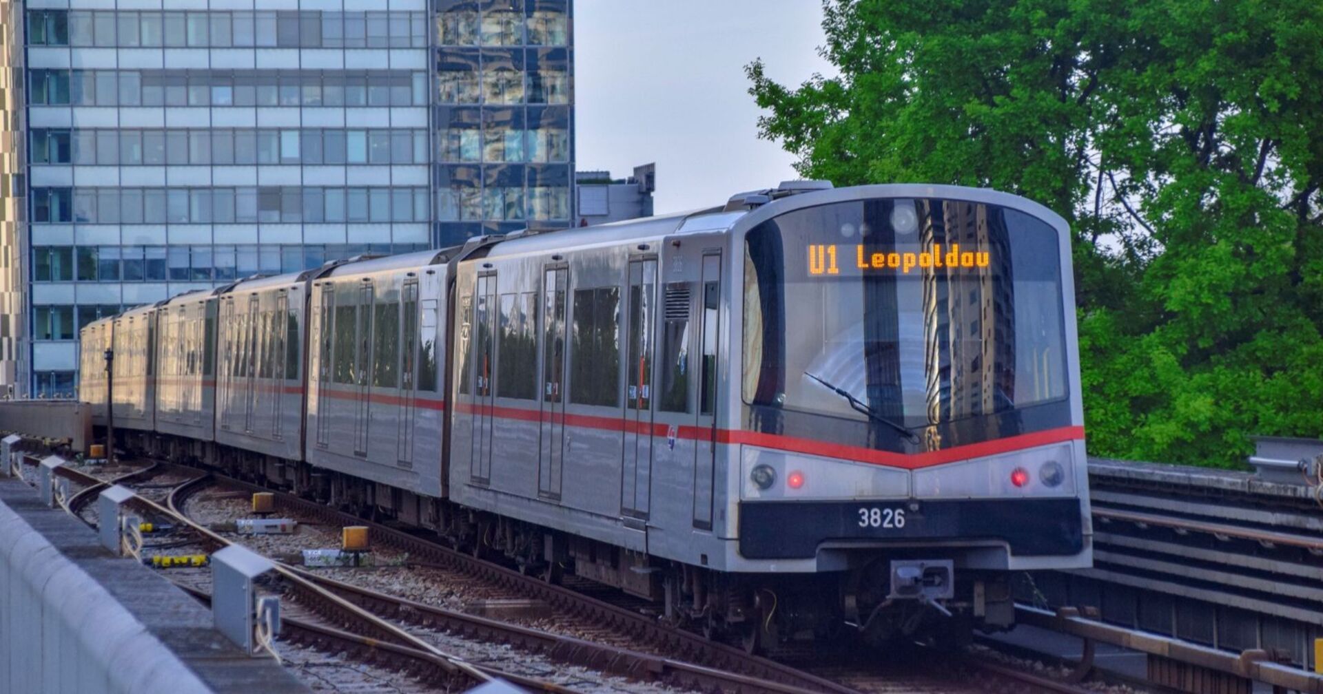 U-Bahn der Linie U1 in Wien auf oberirdischer Strecke, fährt in Richtung Leopoldau, umgeben von modernen Gebäuden und Bäumen.