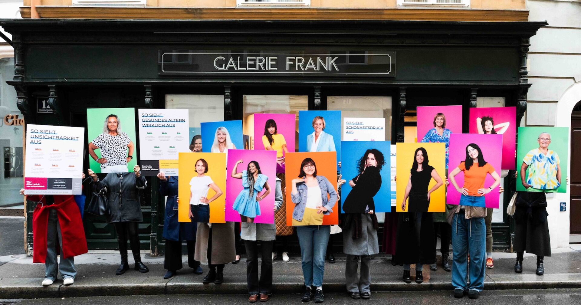 Gruppenbild vor Galerie mit Frauen, die große Porträts von sich hochhalten