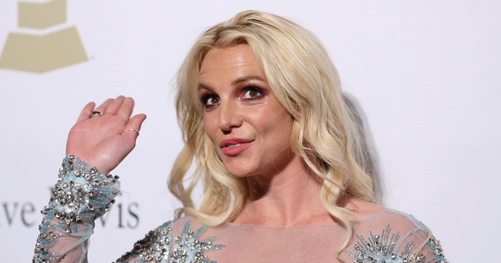 Britney Spears winkt bei einem Auftritt in einem glitzernden, hellblauen Kleid mit silbernen Verzierungen.