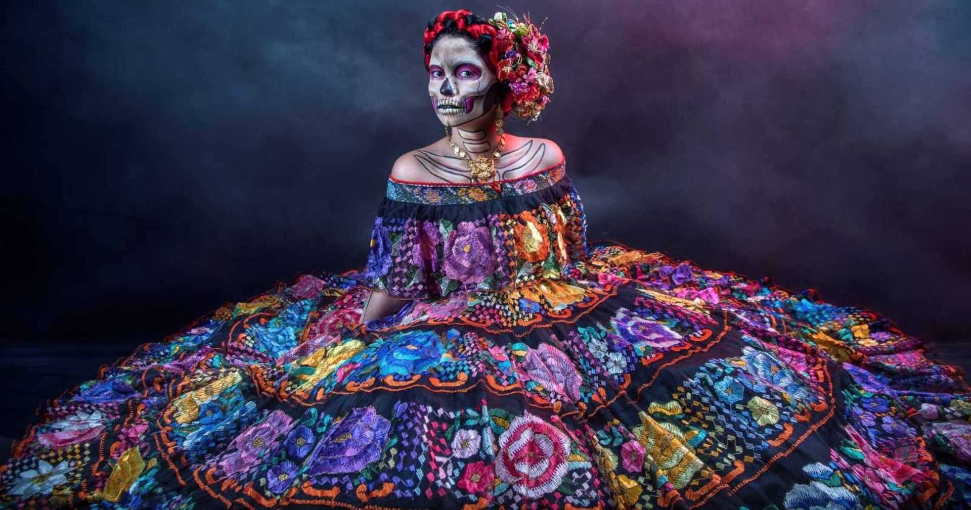 Frau mit kunstvollem Totenschädel-Make-up und farbenprächtigem Kleid zum Día de los Muertos in Mexiko.