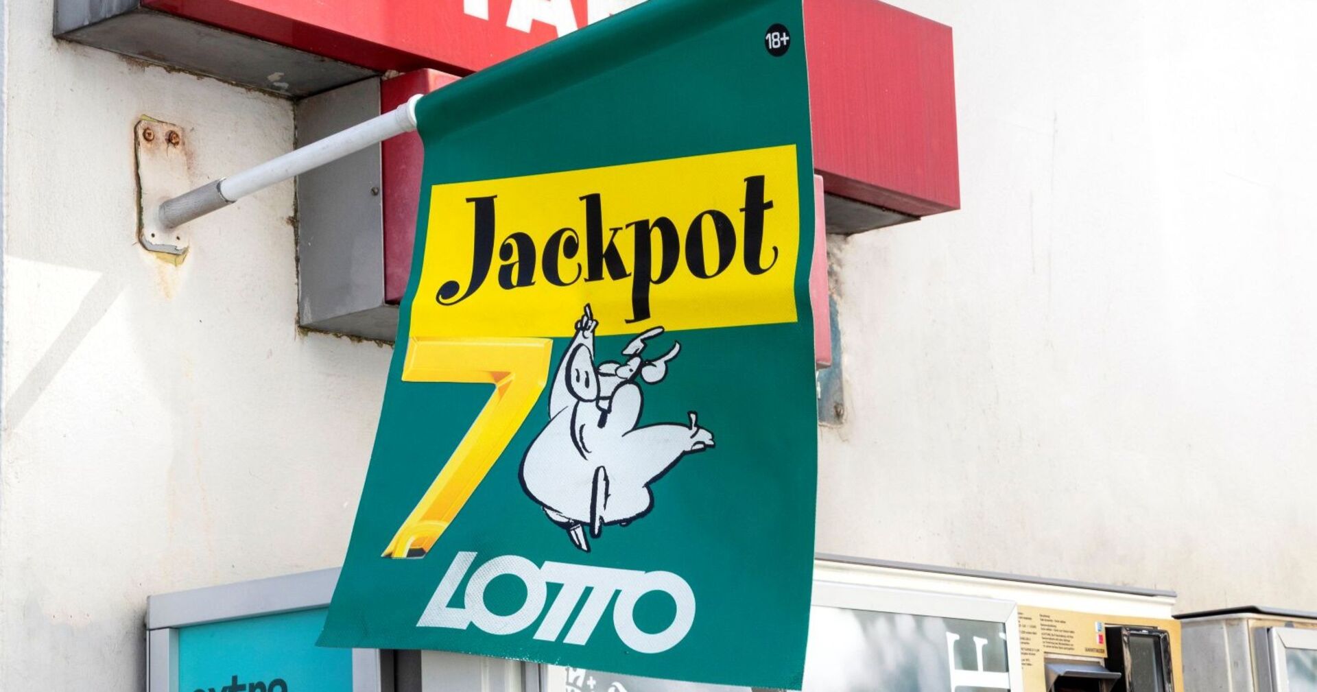 Grünes Lotto-Schild mit der Aufschrift „Jackpot 7“ und Cartoon-Schwein, Symbol für den Millionen-Jackpot.