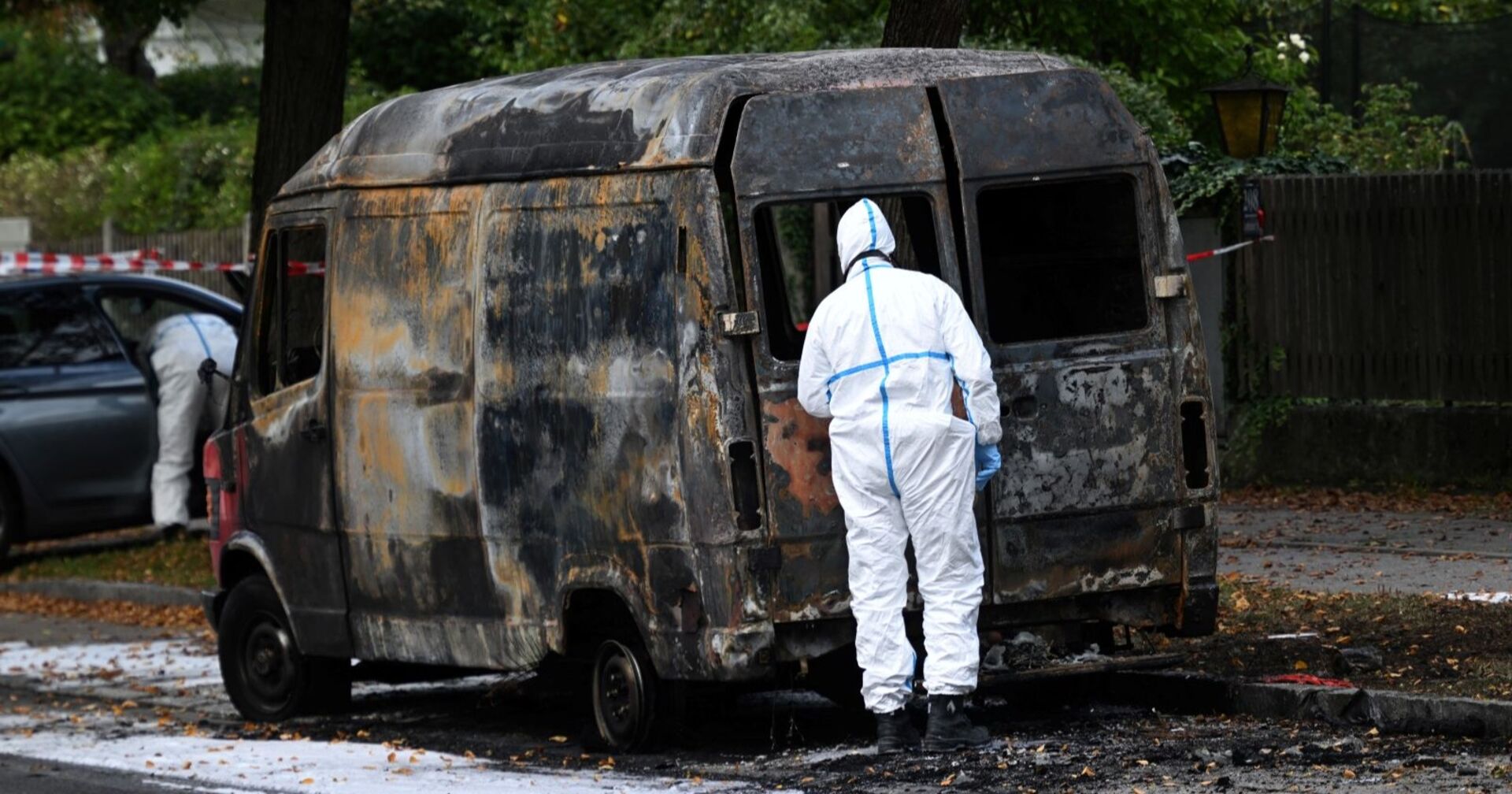 Ausgebrannter Transporter in München-Lerchenau, von Ermittlern in Schutzanzügen untersucht – Teil des Großeinsatzes nach Explosionen und Sprengfallen.