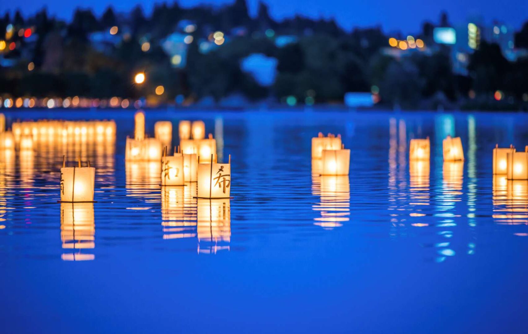 Leuchtende Papierlaternen treiben bei Nacht auf dem Wasser in Japan – Symbol des Gedenkens beim Obon-Fest.