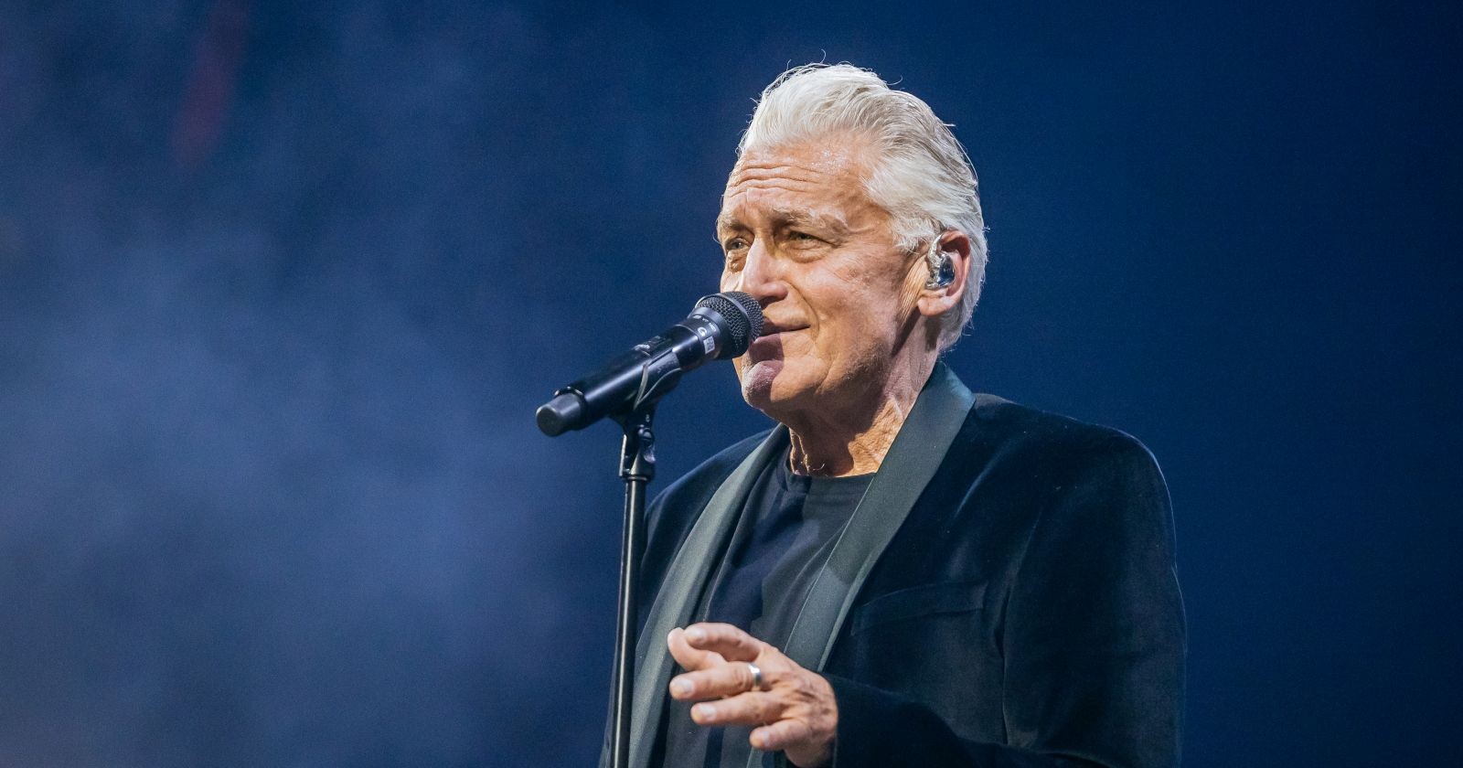 Rainhard Fendrich singt während eines Konzerts in dunkler Kleidung ins Mikrofon.