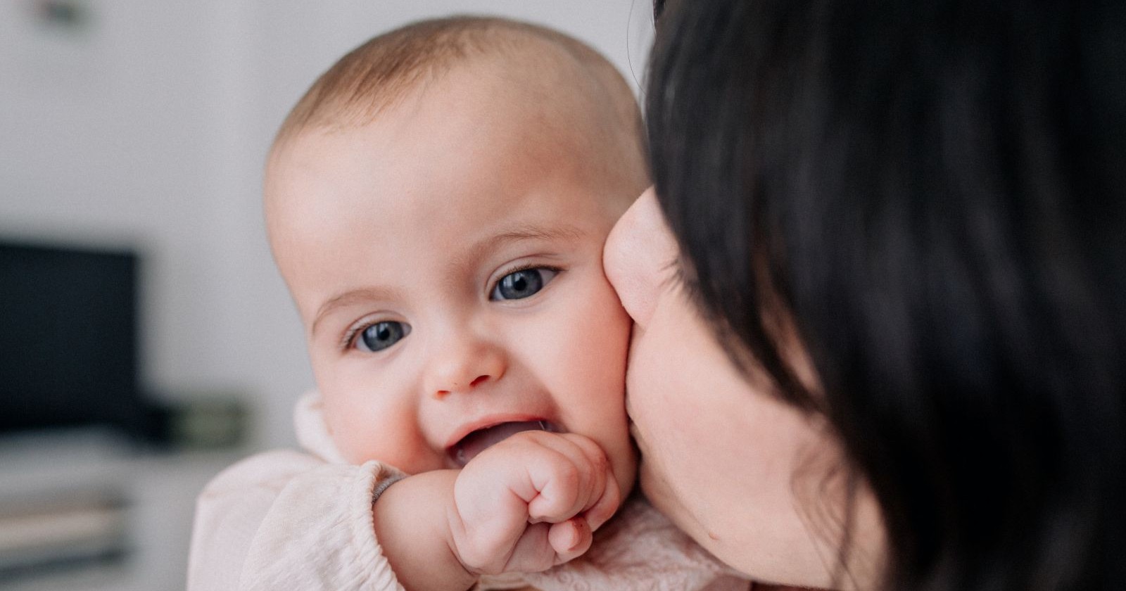 Ein lachendes Baby am Arm einer Frau, sie küsst es - Symbolbild für Social Freezing, das den Kinderwunsch künftig legal auch in Österreich erfüllen kann.