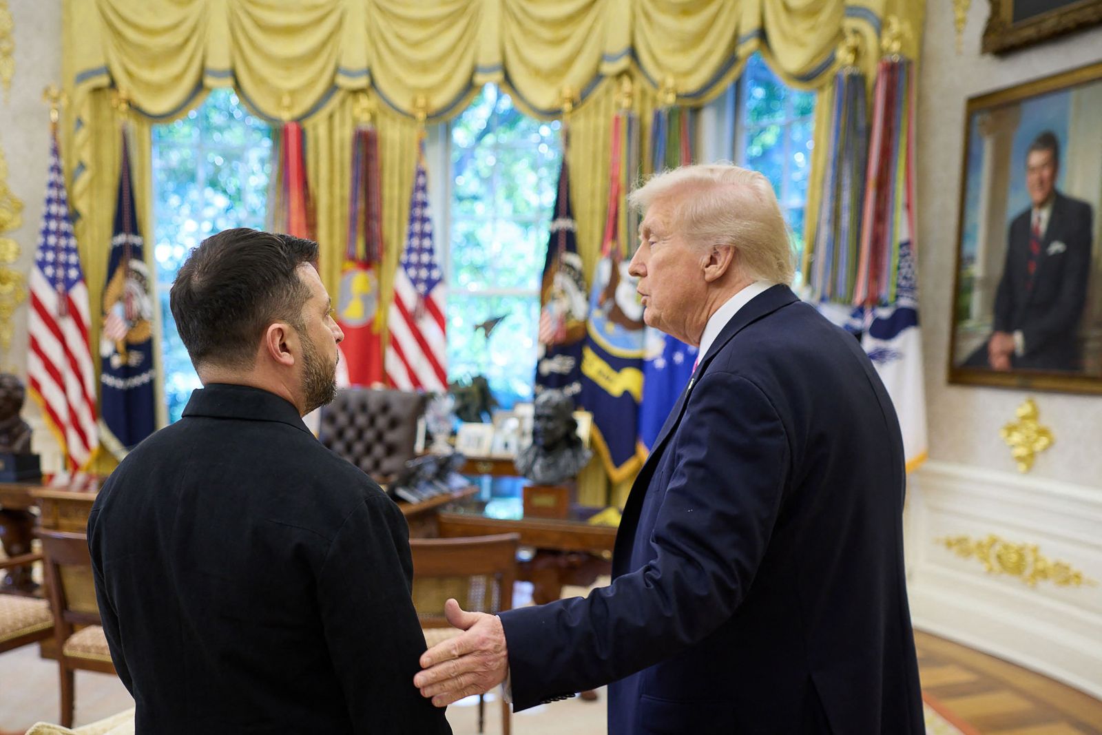 Donald Trump und Wolodymyr Selenskyj stehen im Oval Office des Weißen Hauses und sprechen miteinander, umgeben von US-Flaggen und goldenen Vorhängen.