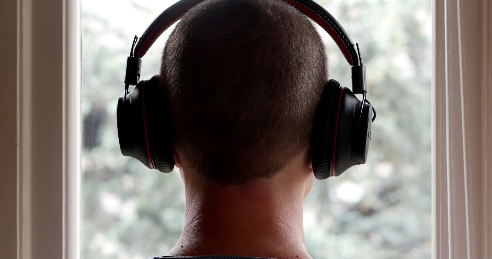 Rückansicht einer Person mit schwarzen Over-Ear-Kopfhörern vor einem Fenster, stellvertretend für den VKI-Schadstofftest bei Kopfhörern.