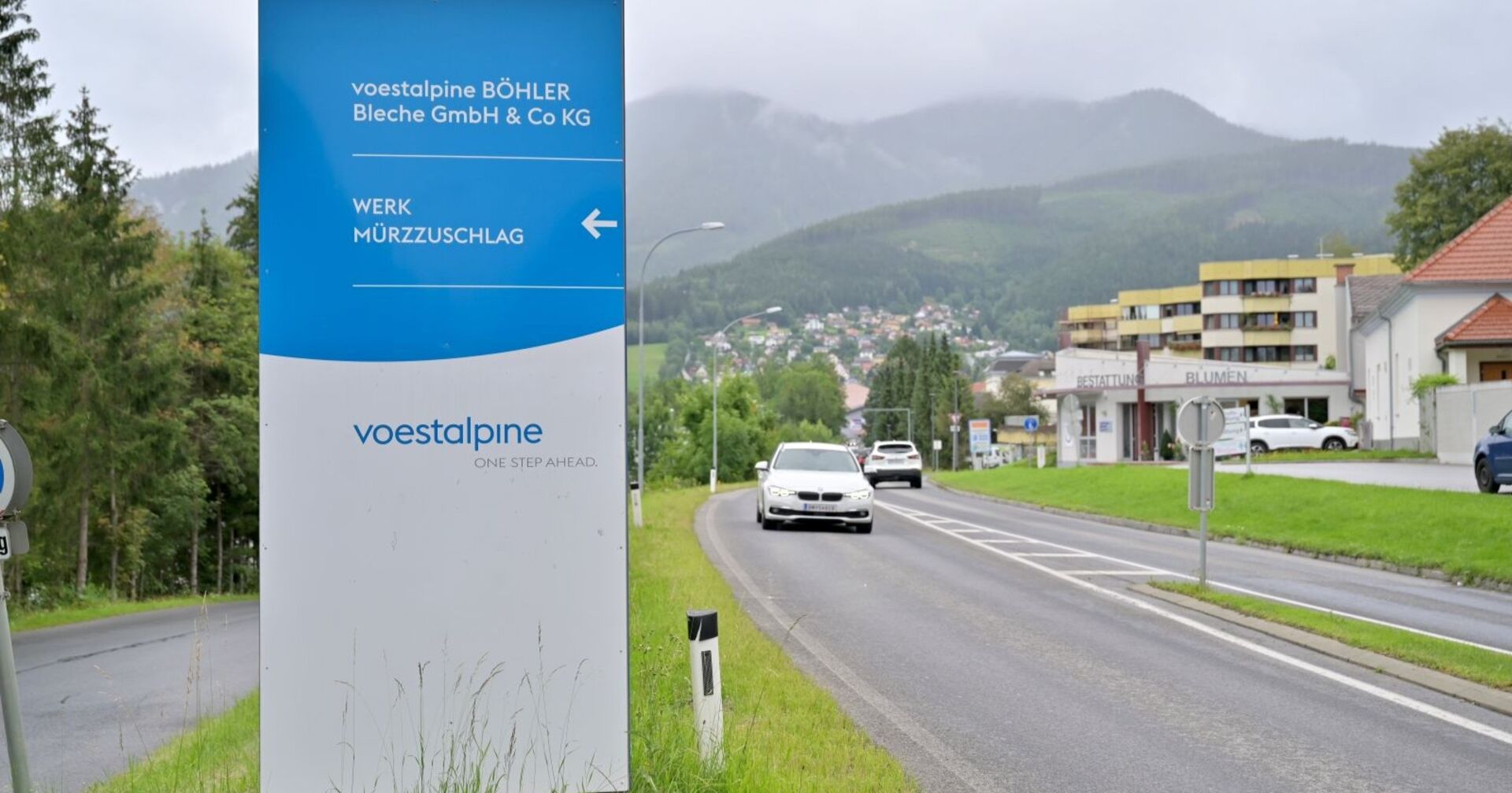 Einfahrtsschild des Voestalpine-Werks Böhler Bleche in Mürzzuschlag mit Blick auf die Straße und die umliegende Stadt im Hintergrund.