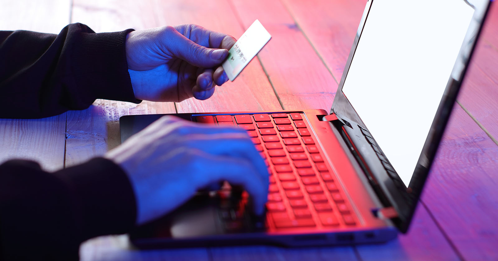 Person vor einem rot beleuchtenden Laptop mit einer Kreditkarte
