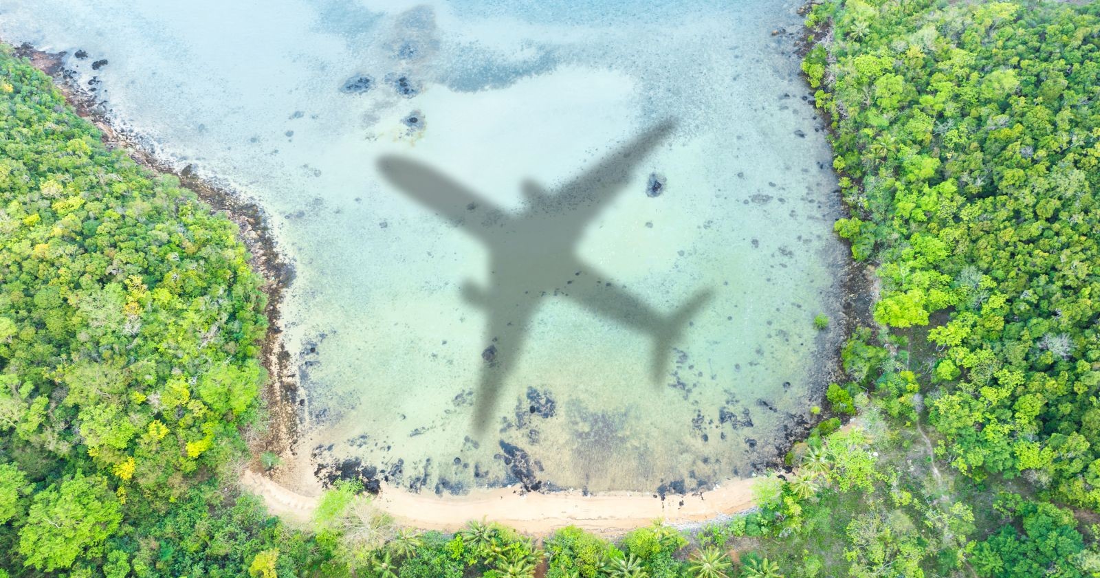Luftaufnahme einer Küste mit grünem Wald und türkisfarbenem Wasser, in dem der Schatten eines Flugzeugs zu sehen ist. Symbolfoto für die Einstellung des Flugbetriebs der Regionalfluglinie Blue Islands.