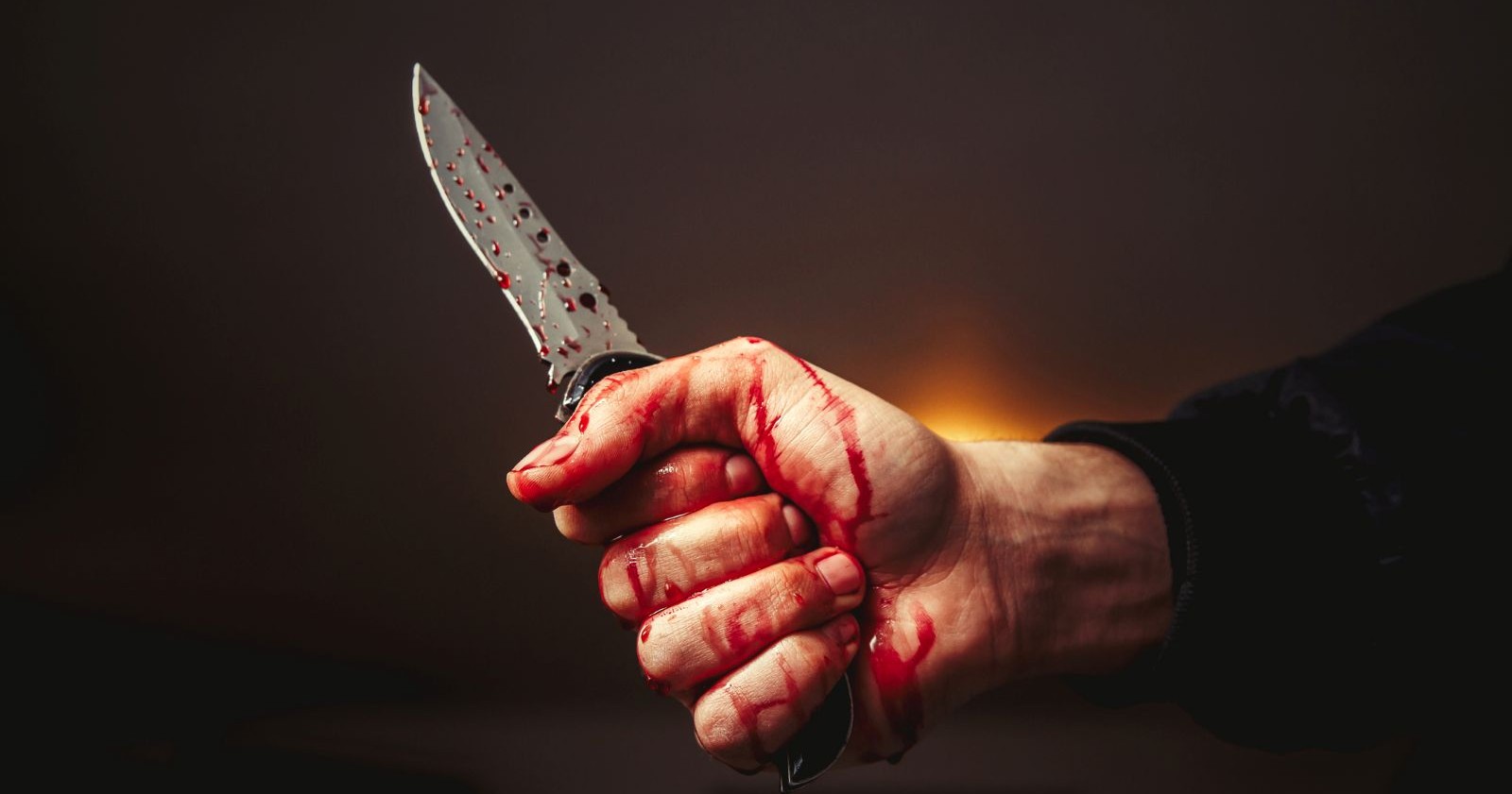 Blutige Hand mit Messer vor dunklem Hintergrund