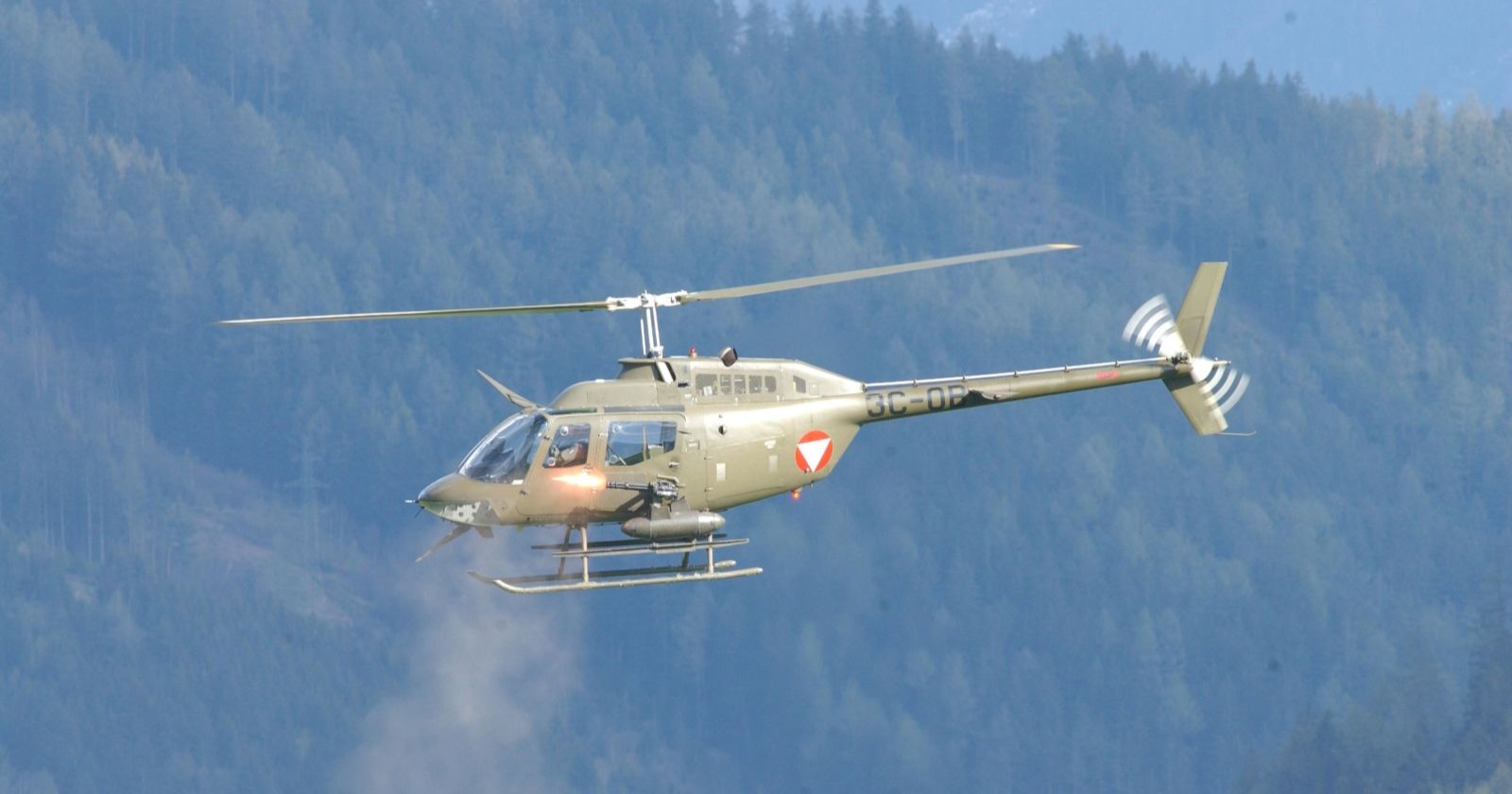 Bundesheer-Hubschrauber Bell OH-58 „Kiowa“ fliegt über bewaldete Hügel, ähnliches Modell wie der in Tulbing notgelandete Helikopter.