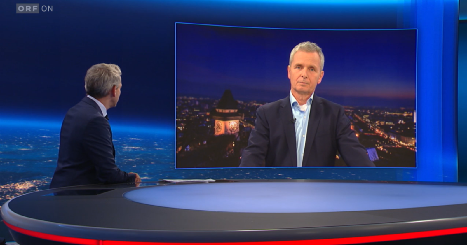 Friedrich Santner spricht per Videozuschaltung in einer Fernsehsendung mit einem Moderator im ORF-Studio über seine neue Rolle als Aufsichtsratsvorsitzender von SOS-Kinderdorf.