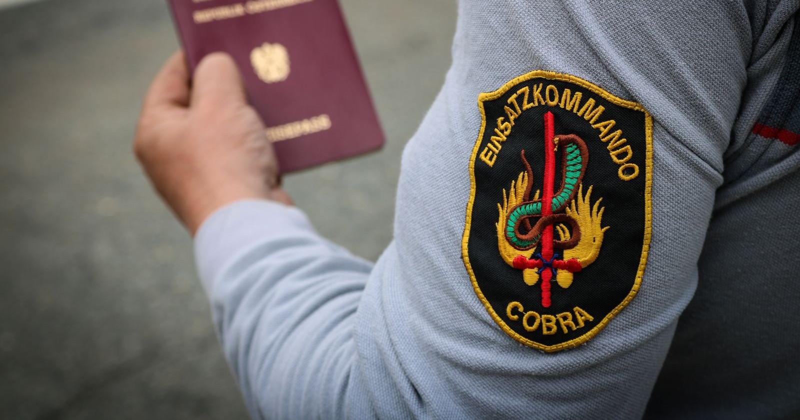 Beamter des Einsatzpolizeikommandos Cobra in Uniform und einem österreichischen Reisepass in seiner Hand
