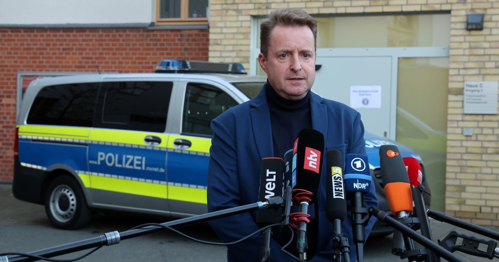 Sprecher der Staatsanwaltschaft Rostock steht vor Mikrofonen und einem Polizeifahrzeug und gibt Informationen zur Festnahme im Fall Fabian (†8).