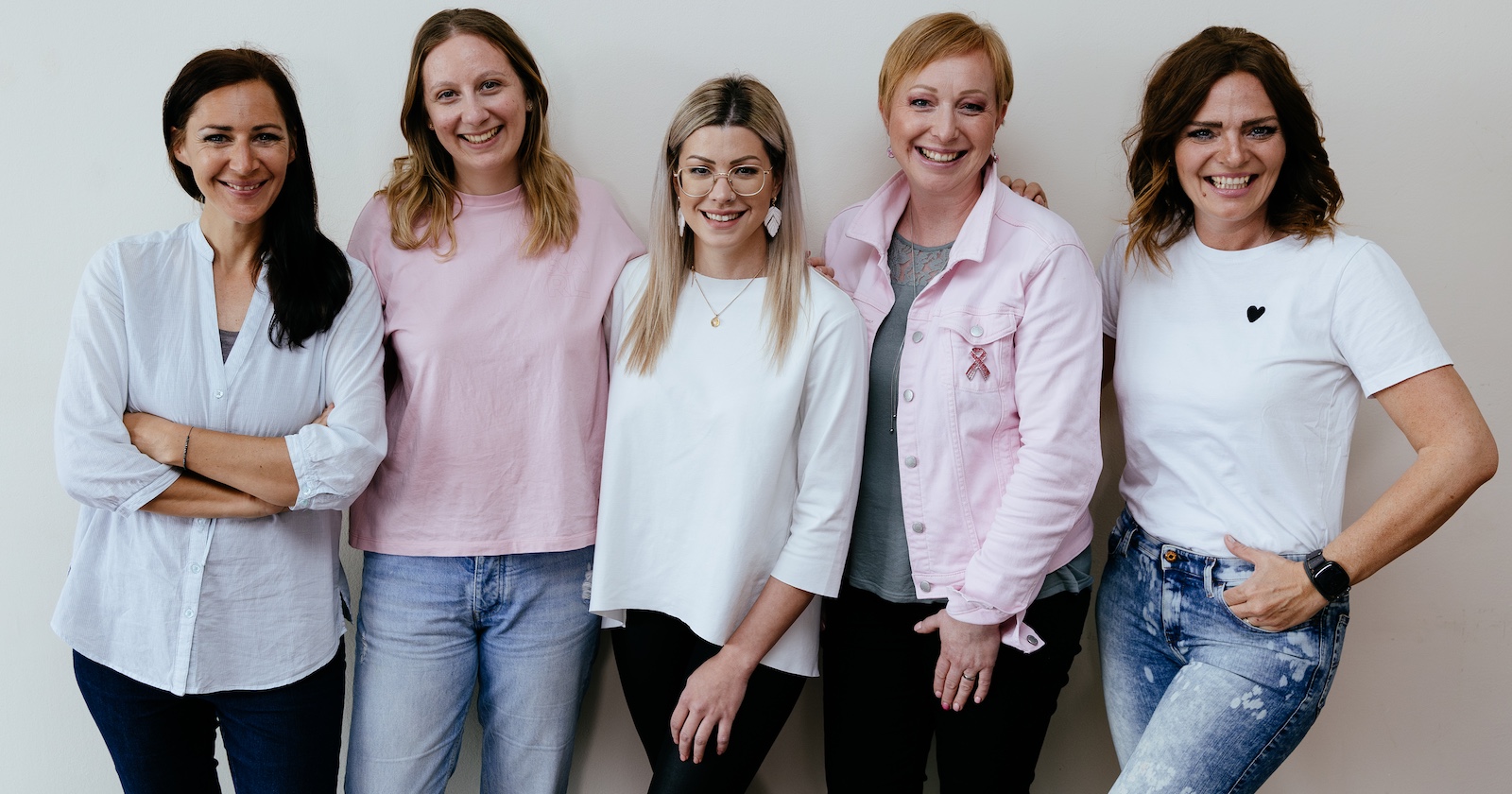 Fünf Frauen in Shirts, Pullovern und Jacken vor einer weißen Wand