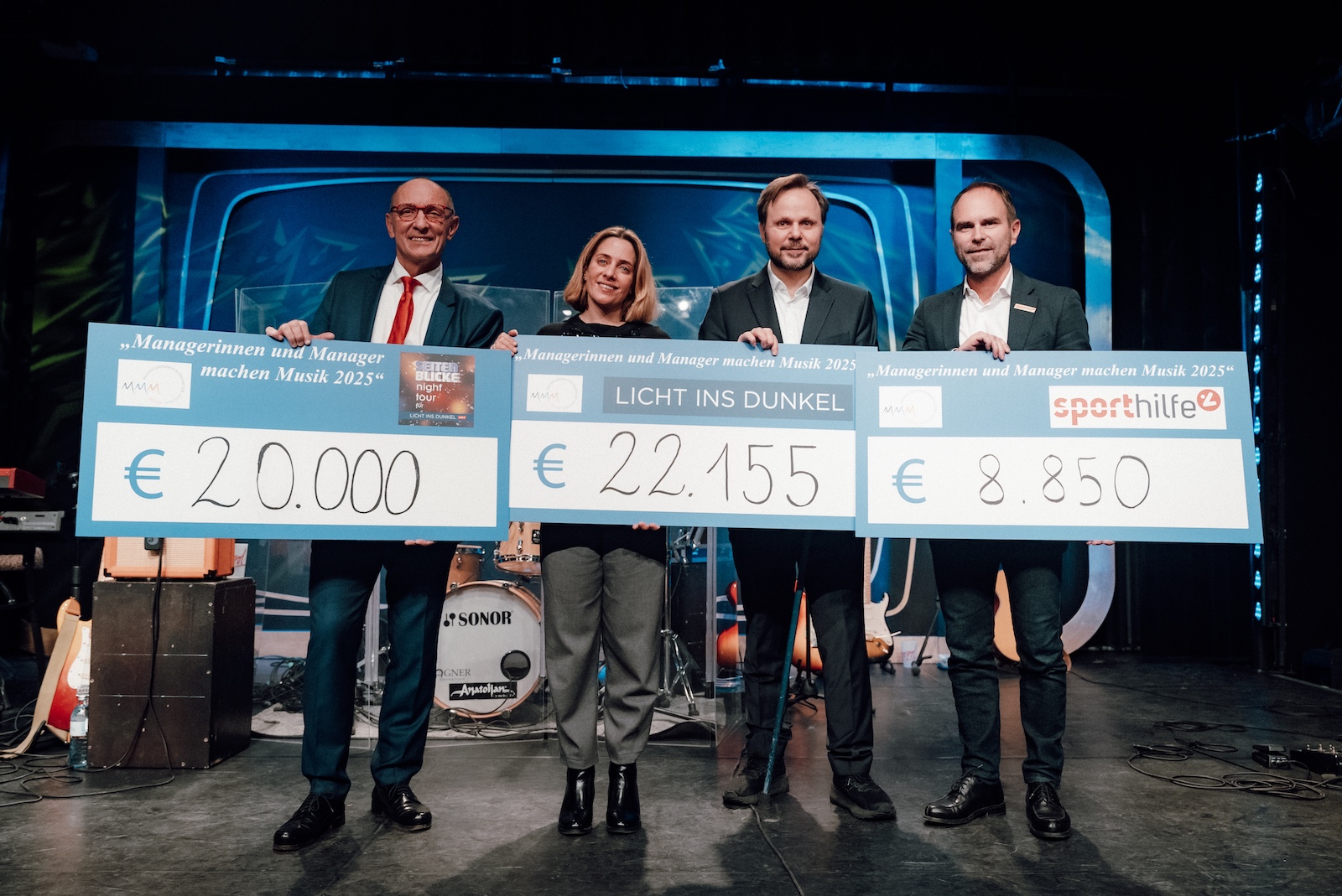 Vier Personen auf Bühne mit symbolischen Schecks