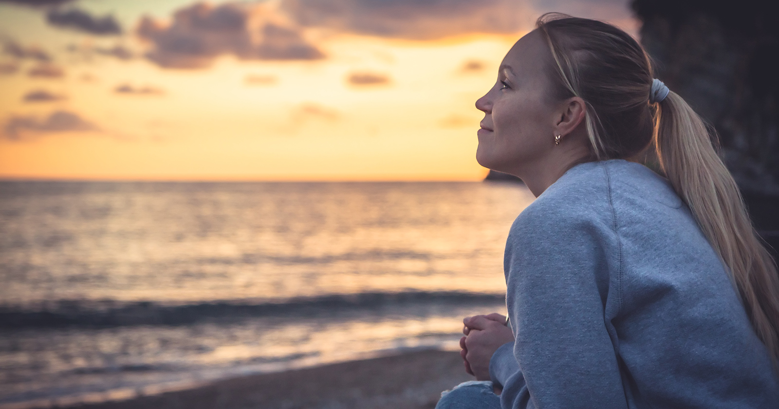 Frau am Strand bei Sonnenuntergang | Credit: iStock.com/splendens