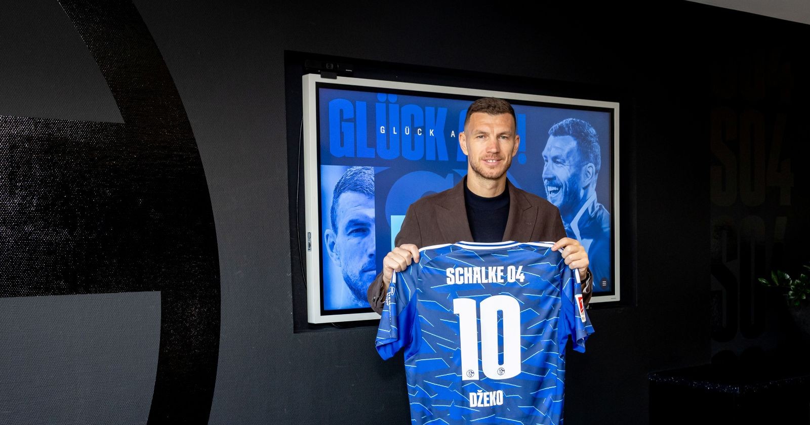 Edin Džeko lächelt bei seiner Vorstellung im Schalke 04 Trikot mit der Rückennummer zehn in der VELTINS-Arena