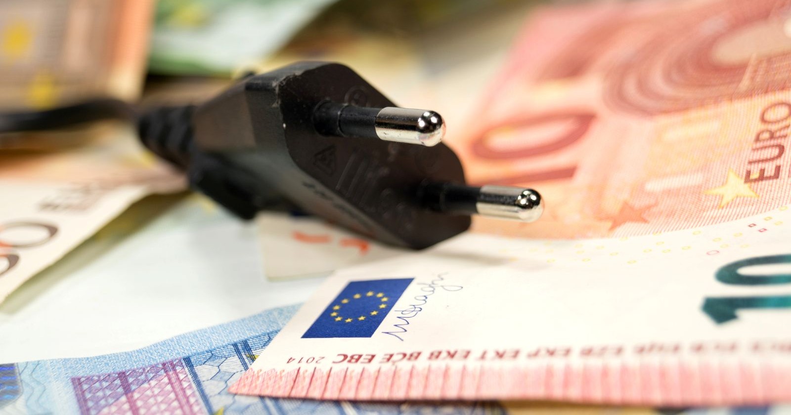 Nahaufnahme eines schwarzen Stromsteckers auf mehreren Euro-Banknoten, Symbolbild für Stromkosten und Preissenkung.