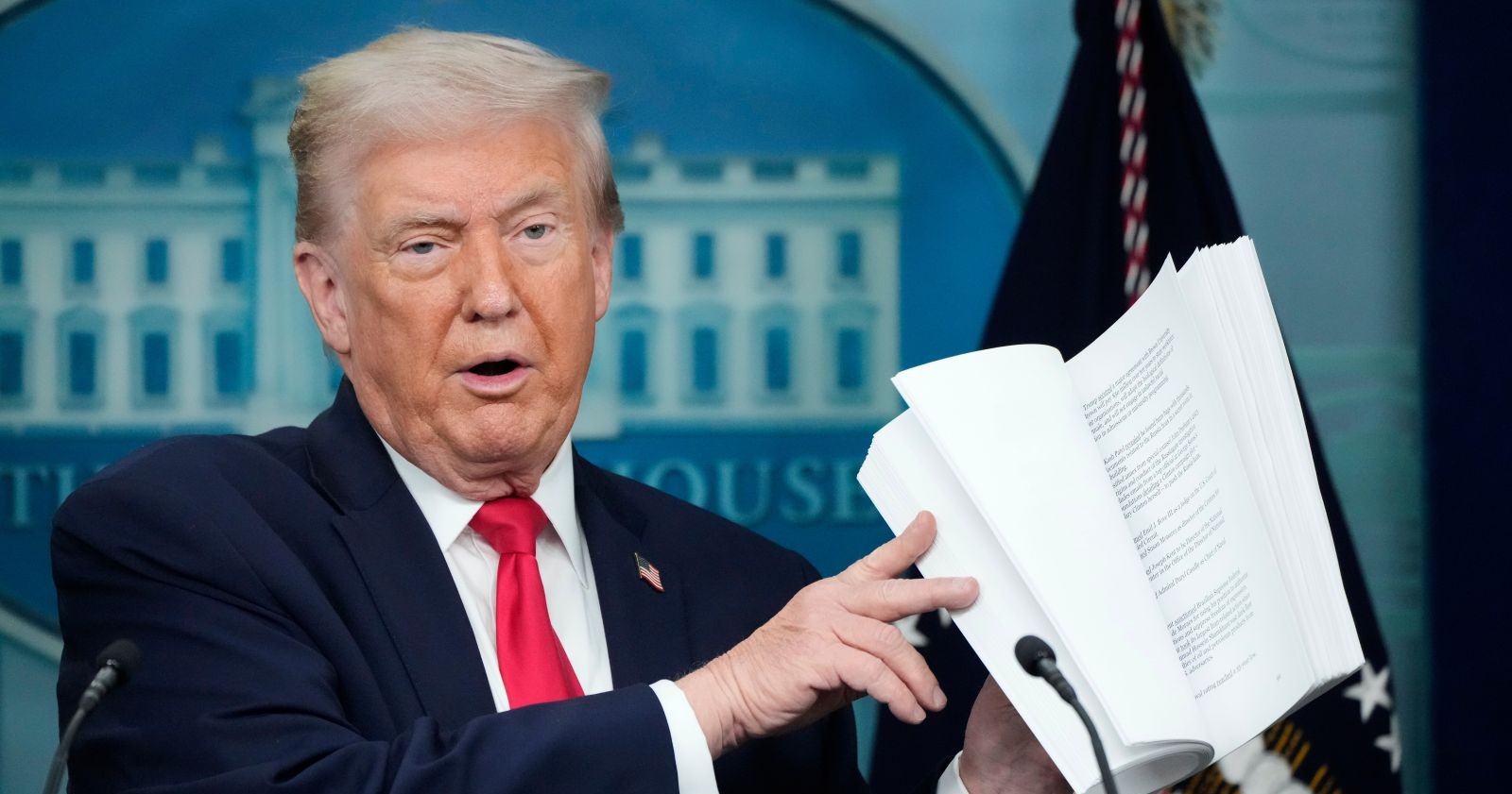 Donald Trump hält ein aufgeschlagenes Dokument in den Händen und erklärt die Inhalte seines geplanten internationalen Friedensrats im Weißen Haus.