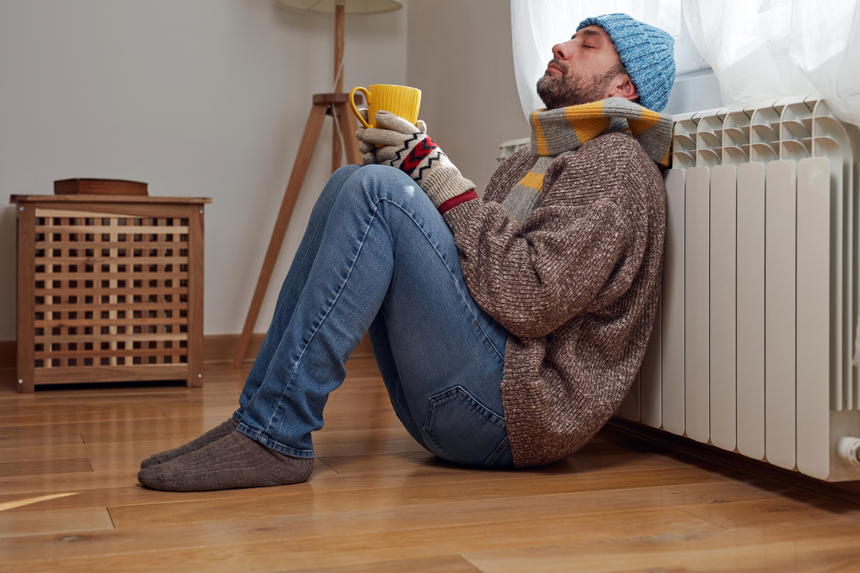 Mann mit Erkältung sitzt mit Tee vor einer Heizung