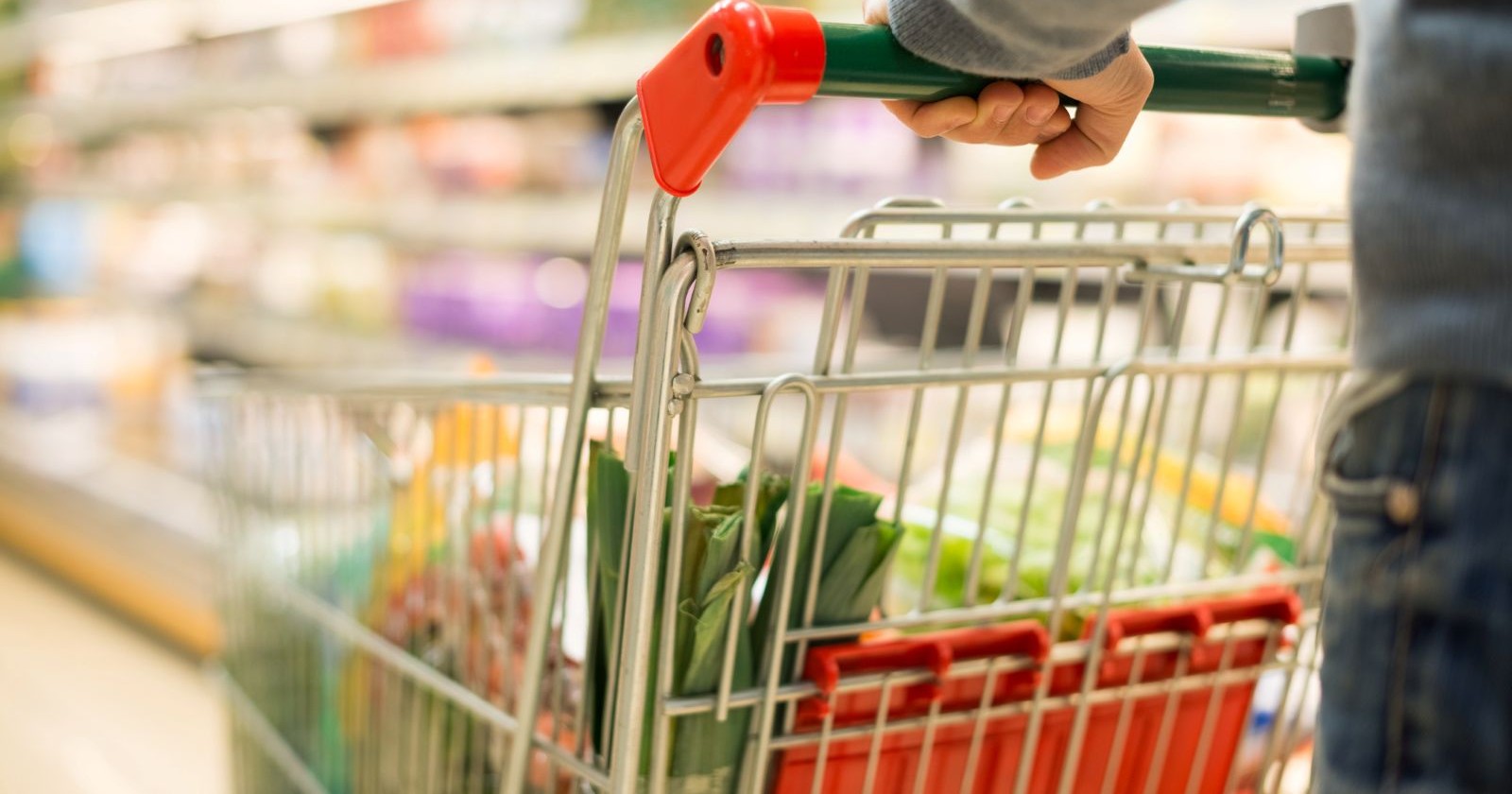Mann in einem Supermarkt, mit einem gefüllten Einkaufswagen, in welchem sich Lebensmittel befinden