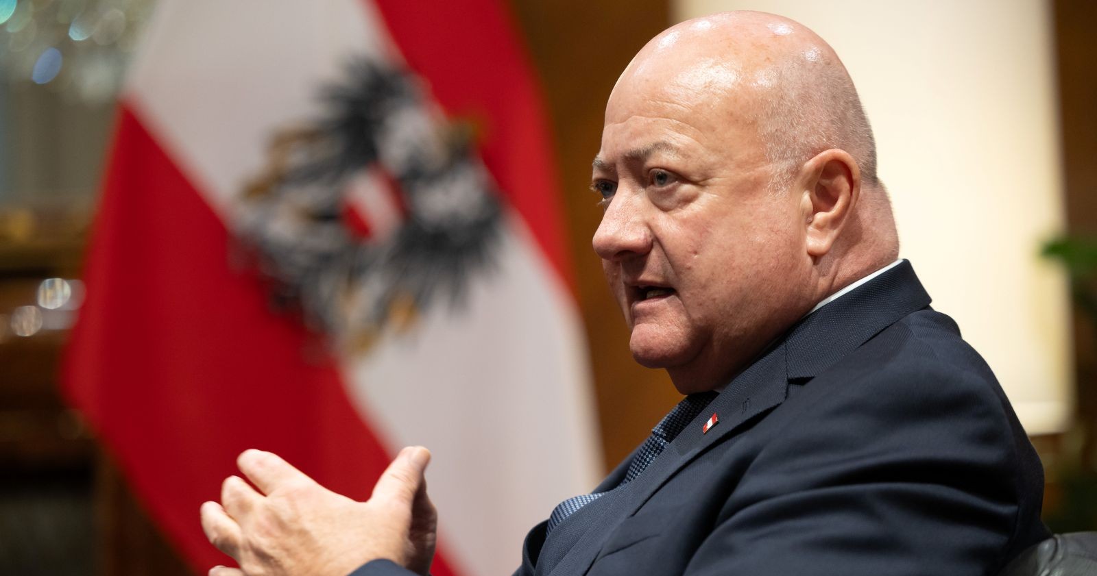 Österreichs Bundeskanzler Christian Stocker spricht im Bundeskanzleramt, im Hintergrund die österreichische Flagge.