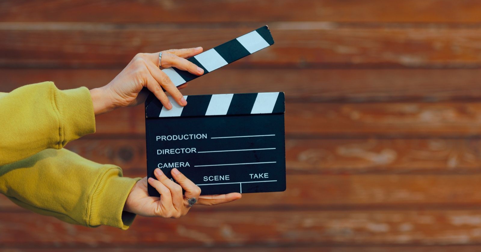 Hand, die eine Filmschiefertafel auf Holzhintergrund häl