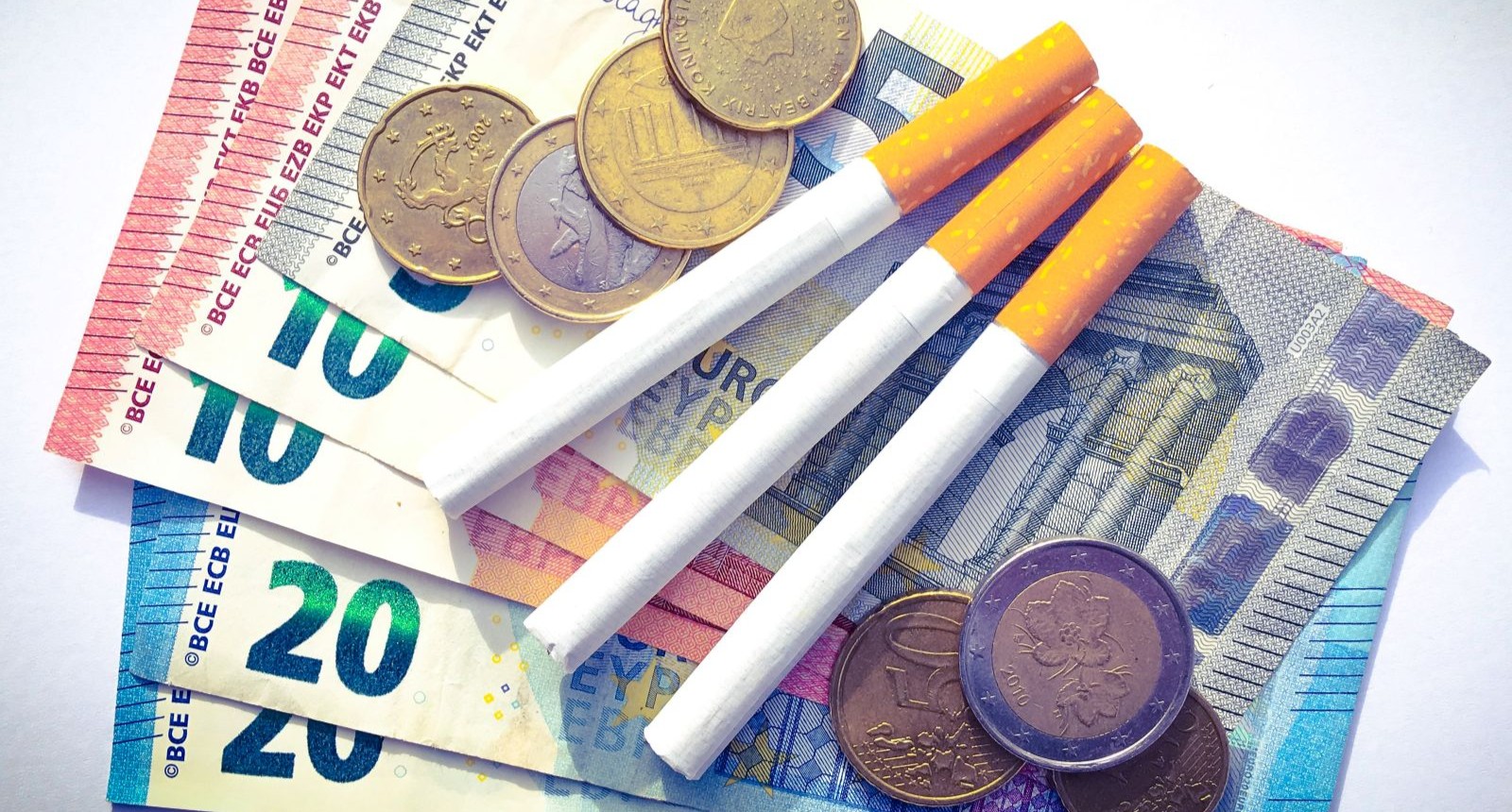 Zigaretten liegen auf Euro-Geldscheinen und Münzen – Symbolbild zur Zigaretten-Preiserhöhung in Österreich.