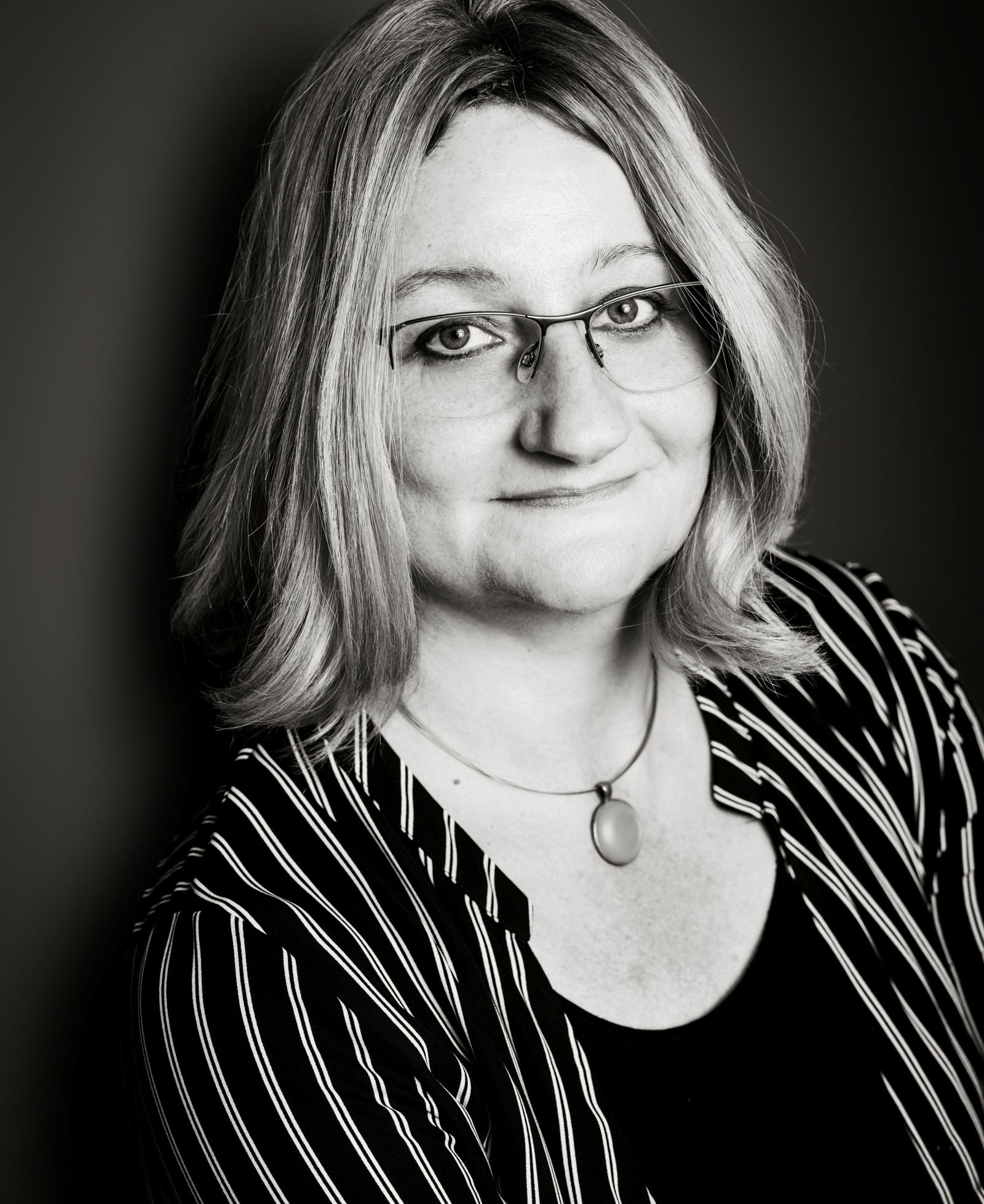 Frau mit halblangen Haaren, gestreifter Bluse und Brille