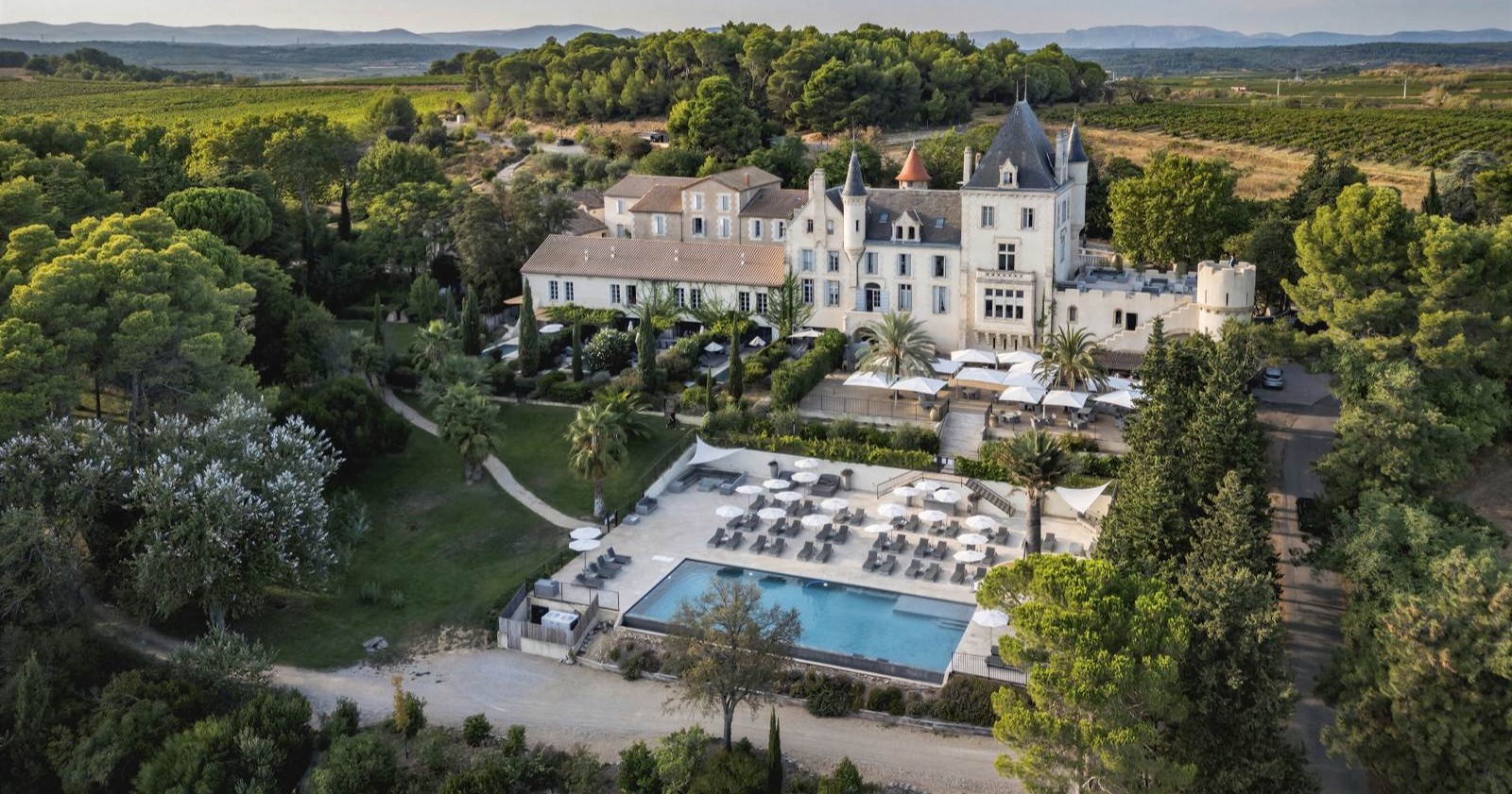 Luftaufnahme von Château Les Carrasses in Südfrankreich mit Pool, Parkanlage und Weinbergen in der Umgebung.
