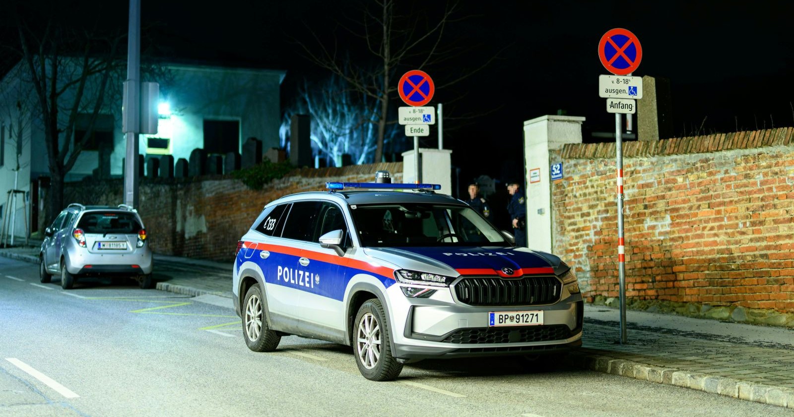 Ein Polizeiauto steht nachts vor einer Mauer nahe dem Friedhof Baumgarten in Wien, wo eine 64-jährige Frau getötet wurde. Die festgenommene Verdächtige (14) ist geständig