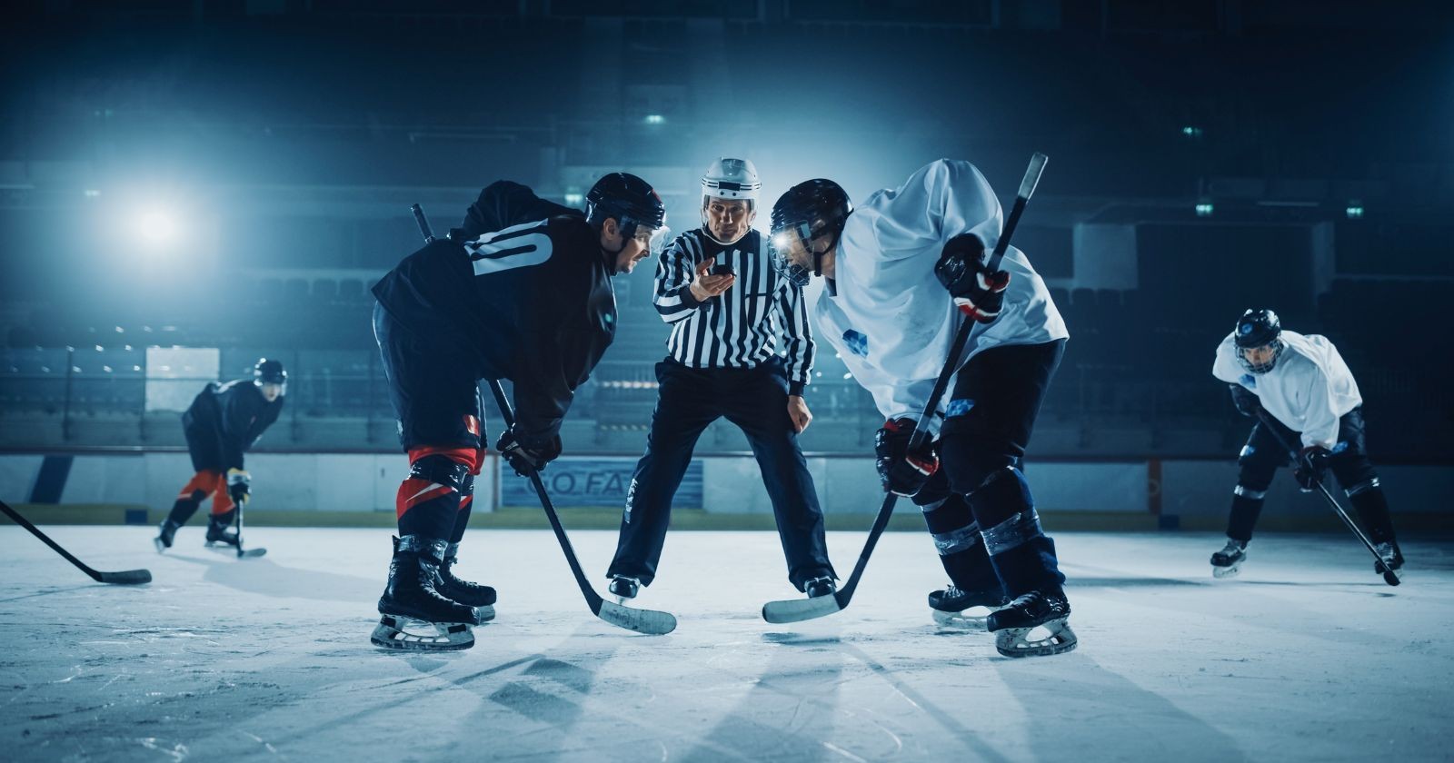 Zwei Eishockeyspieler stehen sich am Eis gegenüber, in der Mitte steht ein Schiedsrichter