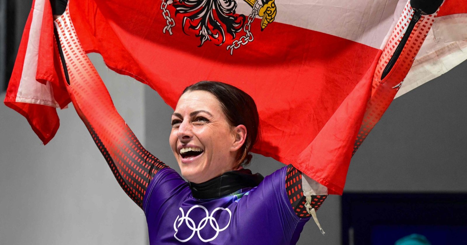 Janine Flock feiert in Cortina d’Ampezzo ihren Olympia-Sieg im Skeleton und hält die österreichische Fahne über sich.