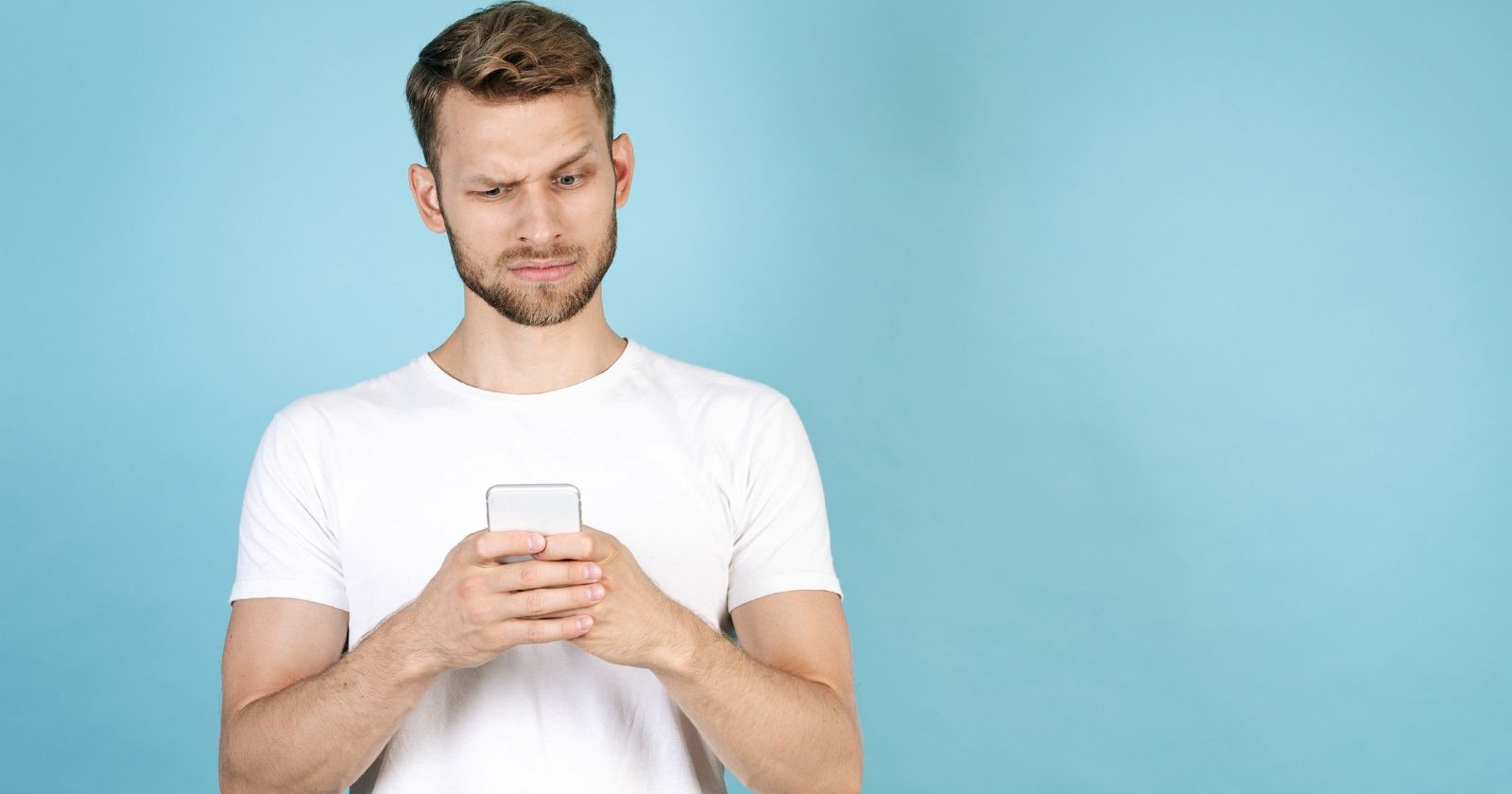 junger Mann im weißen T-Shirt blickt skeptisch auf sein Handy