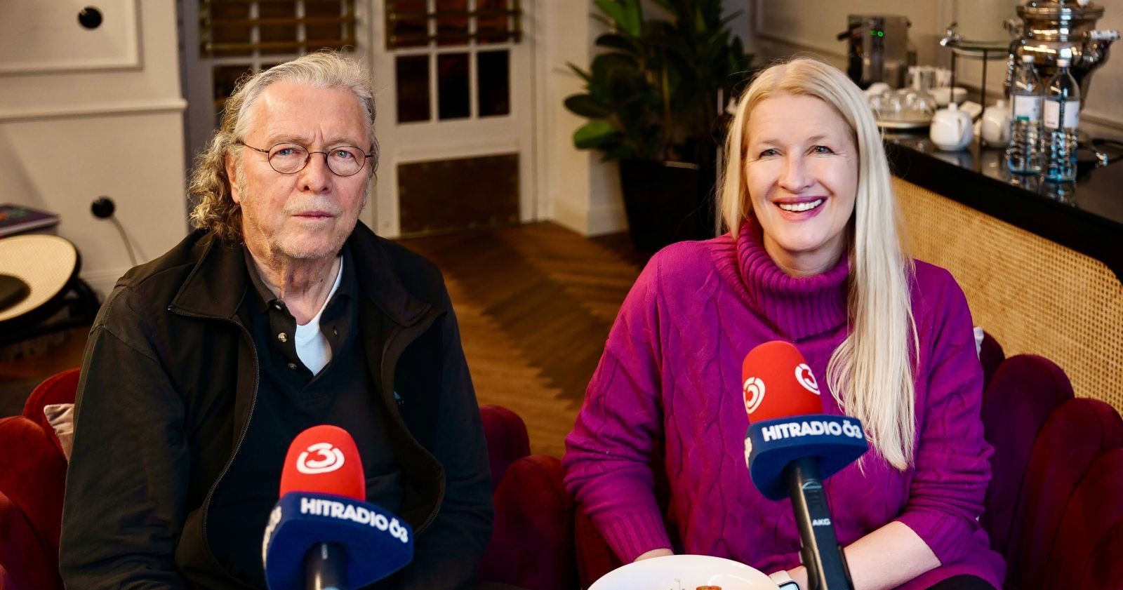 Peter Cornelius und Claudia Stöckl sitzen während des Interviews für Ö3 „Frühstück bei mir“ nebeneinander vor Mikrofonen im Studio.