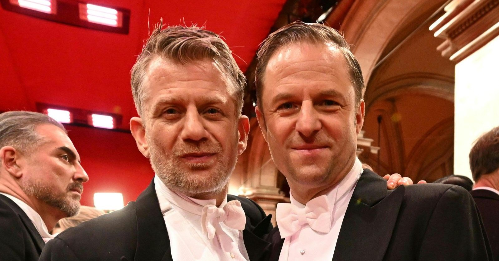 Philipp Hochmair und Andreas Guenther posieren im Frack beim Wiener Opernball und lächeln in die Kamera.