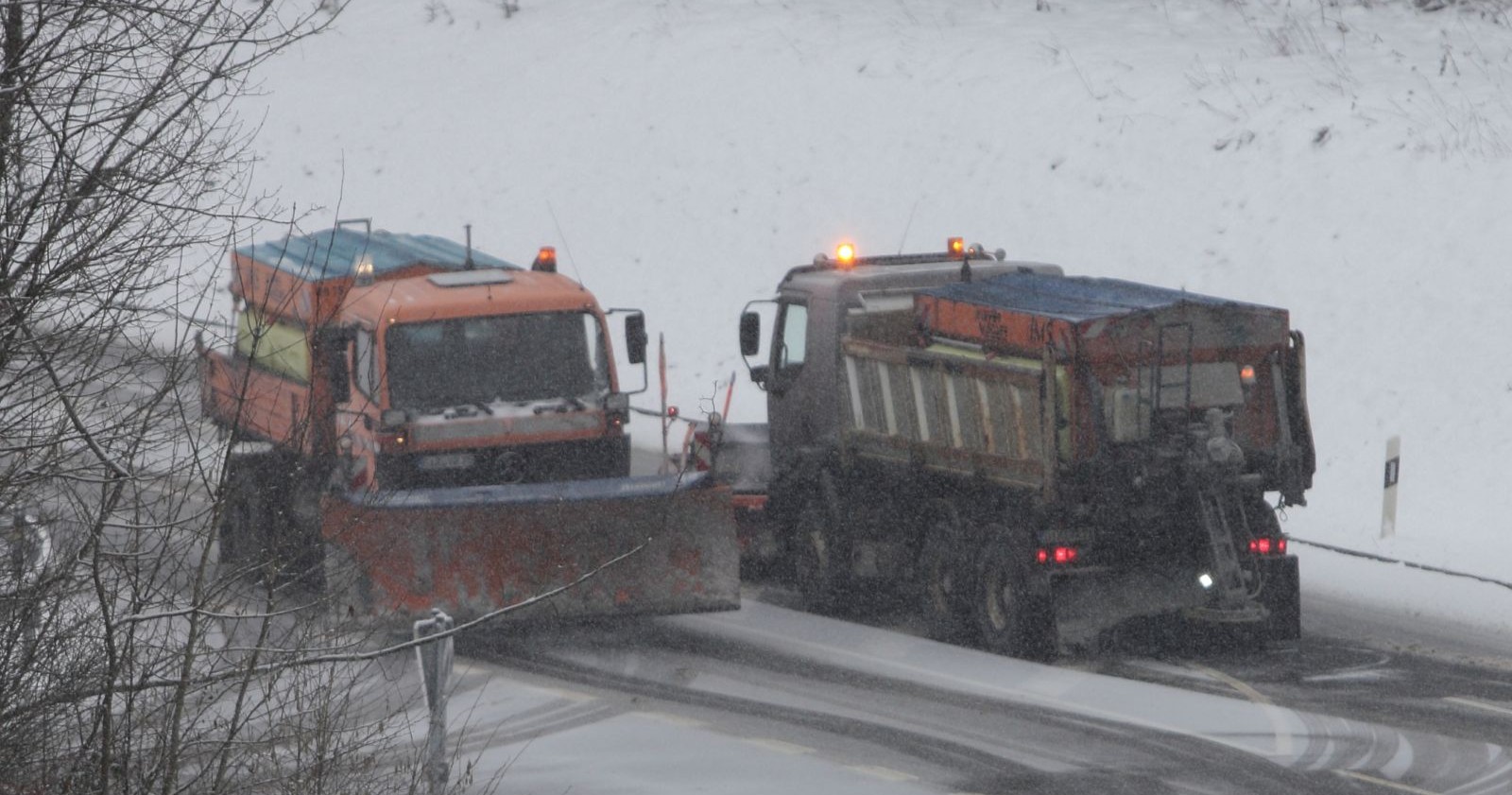 Zwei Schneepflüge räumen eine schneebedeckte Straße in Kärnten während anhaltendem Schneefall.