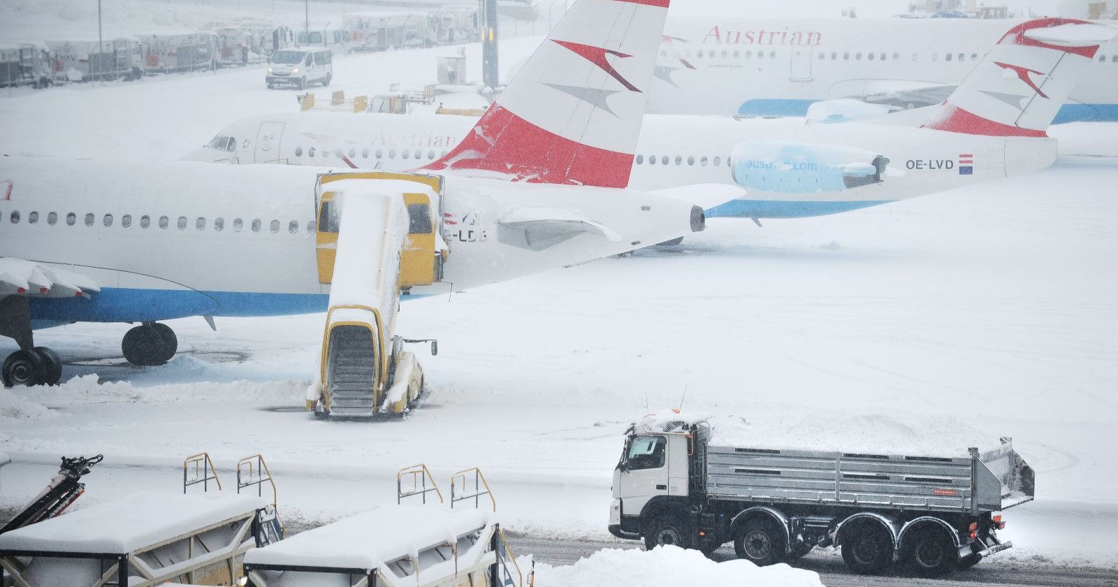 Verschneite Flugzeuge am Flughafen Wien-Schwechat, während Räumfahrzeuge versuchen, die Startbahnen von Schnee zu befreien.