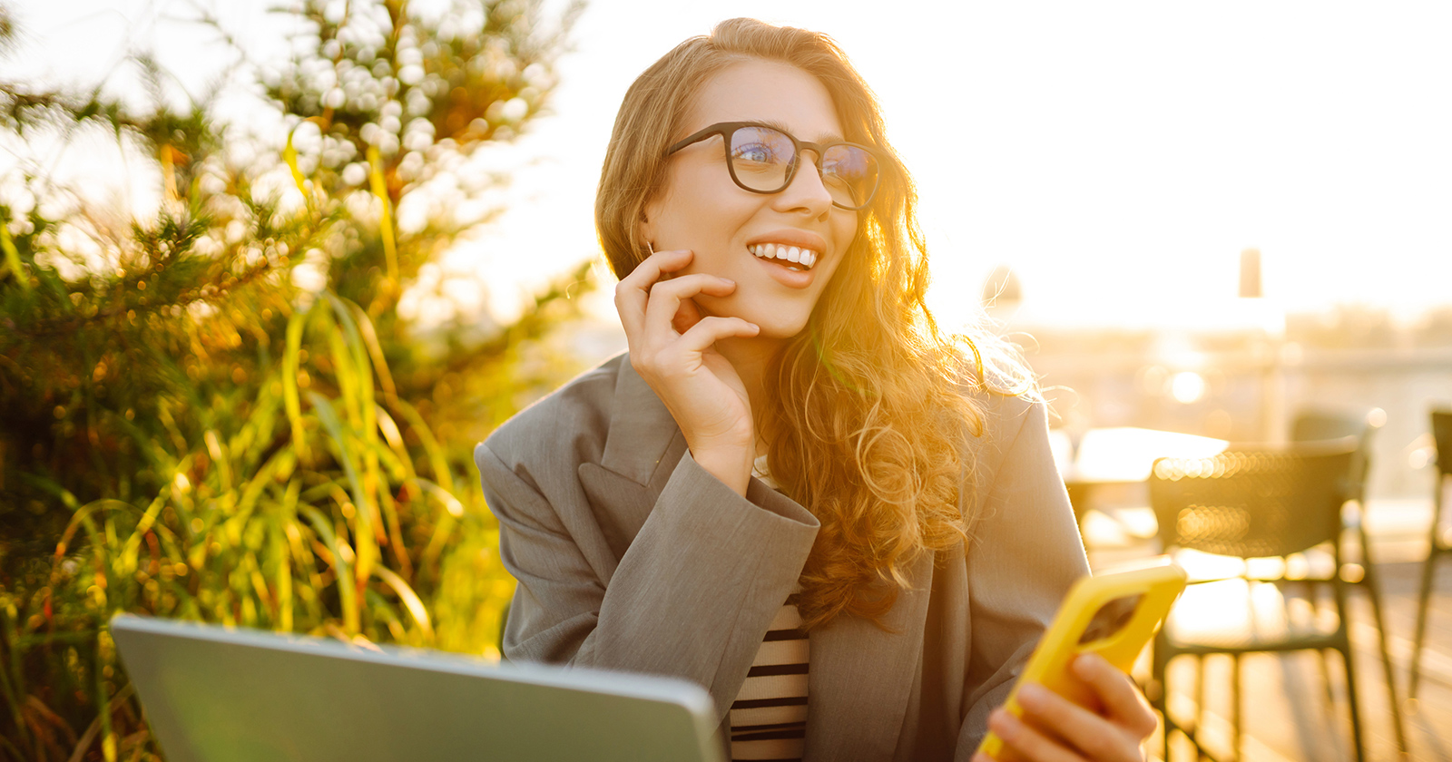 Junge gut gelaunte Frau mit Smartphone in der Hand vor ihrem Notebook | Credit: iStock.com/Maksym Belchenko