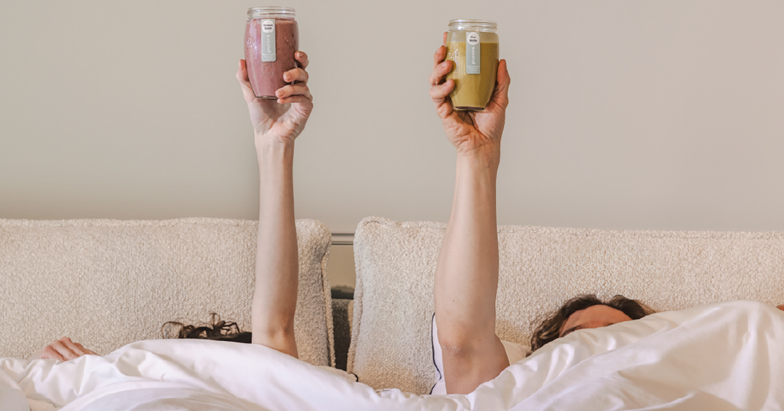 Pärchen unter der Decke hält Gläser mit gesunden Säften hoch | Credit: Monika Löff