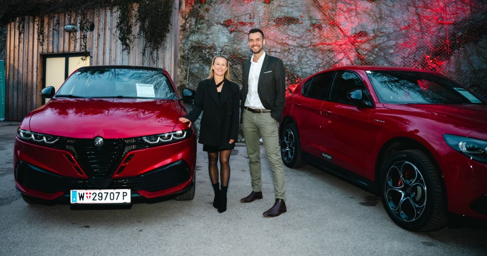 Gastgeberin und Wirtschaftspartner vor zwei roten Autos