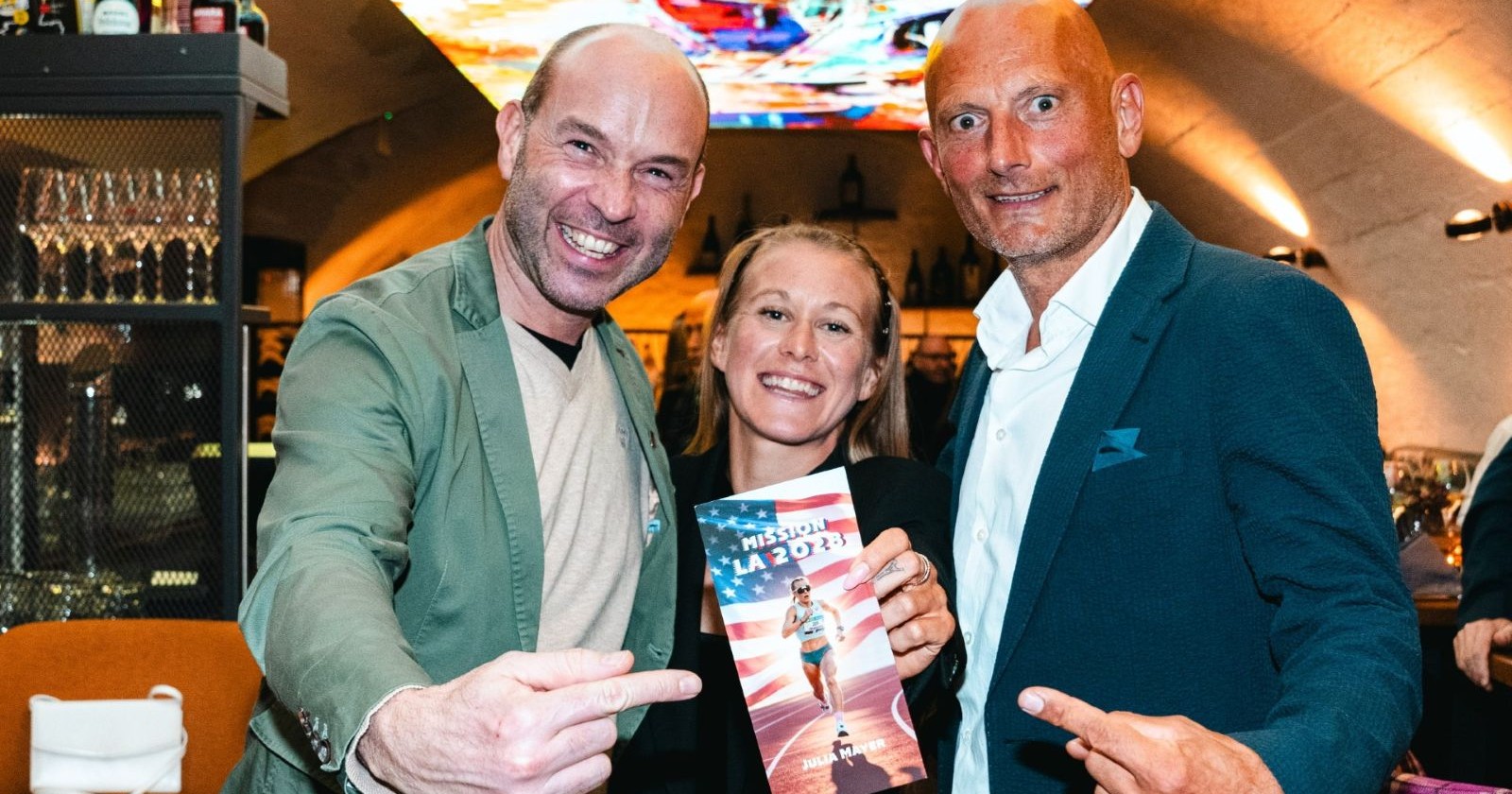 Trio hält Broschüre der Marathon-Rekordhalterin in die Kamera