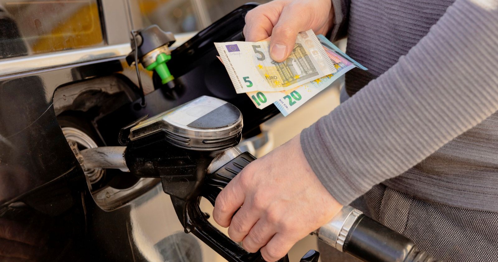 Person tankt ein Auto und hält Euro-Scheine in der Hand. Symbolbild für Spritpreise, Diesel, Super und Sparen beim Tanken.