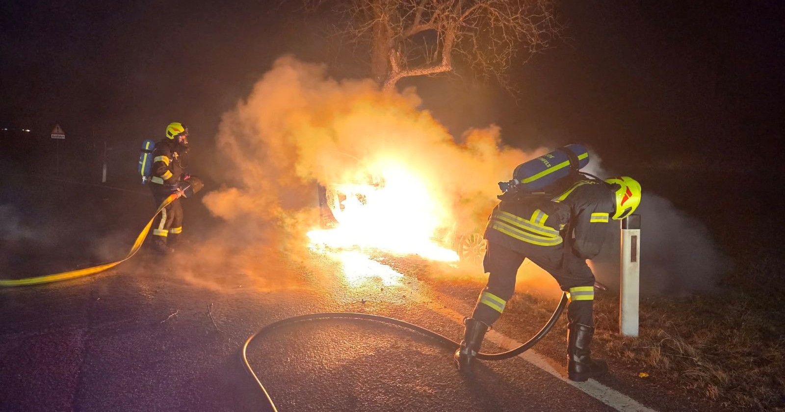 Einsatzkräfte der Feuerwehr Frankenfels bei Löscharbeiten an einem ausgebrannten Pkw, der gegen einen Baum geprallt ist