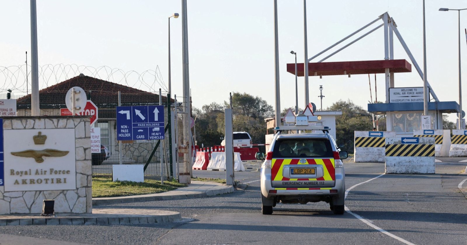 Einfahrt des britischen Royal-Air-Force-Stützpunkts Akrotiri auf Zypern mit Sicherheitsabsperrungen, Warnschildern und einem Einsatzfahrzeug.