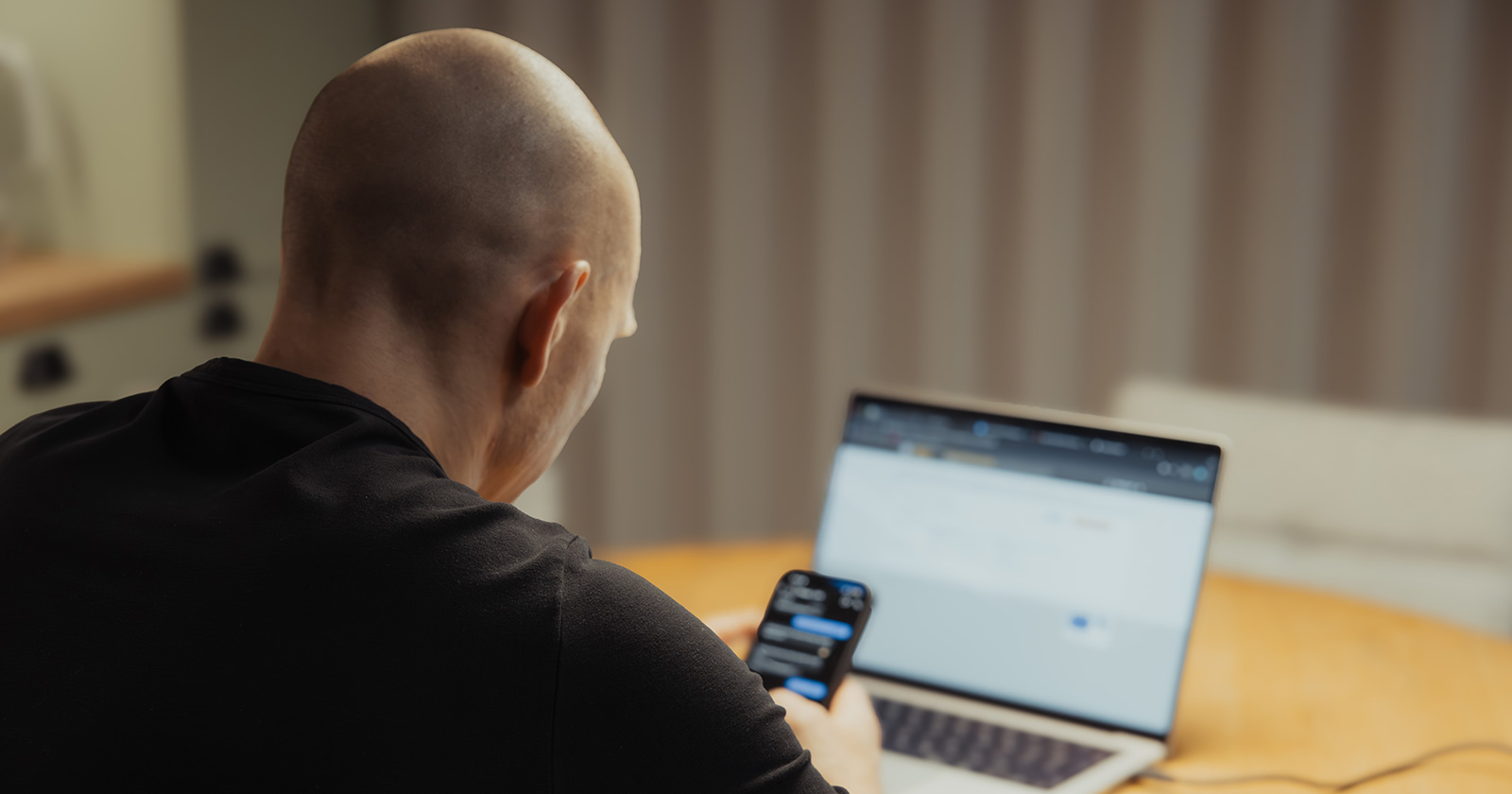 Mann hinter dem Laptop mit Smartphone in der Hand | Credit: TimelessNordic/Shutterstock