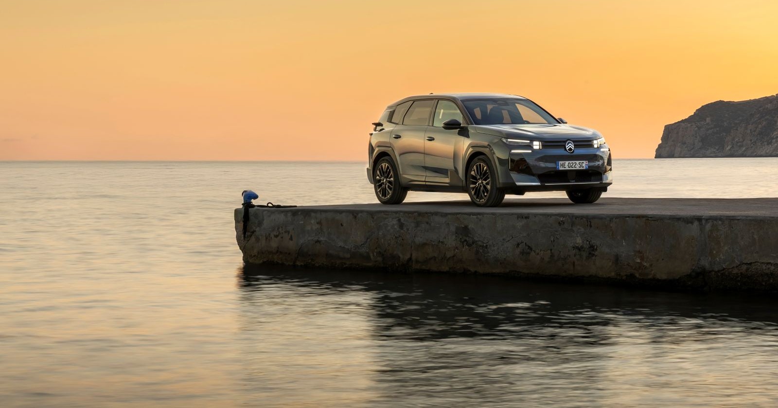 Ein Citroën ë-C5 Aircross parkt auf eine Mole. Man sieht das ruhige Meer und im Hintergrund scheint die Sonne unterzugehen.